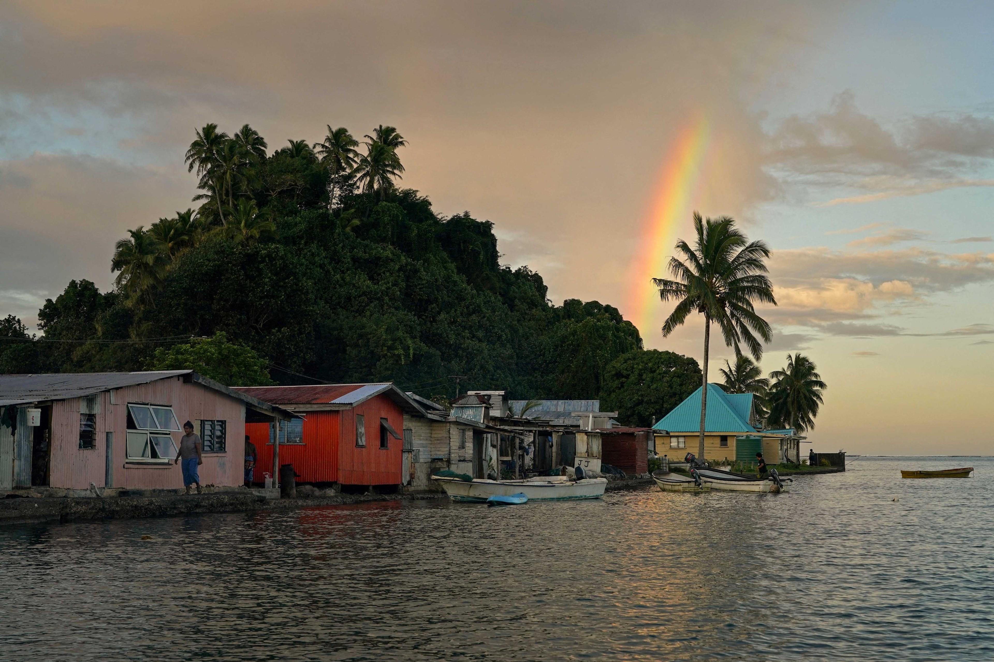 A local resident walks along a sea wall, as a rainbow forms over Serua Village, Fiji, July 14, 2022. Photo: Reuters