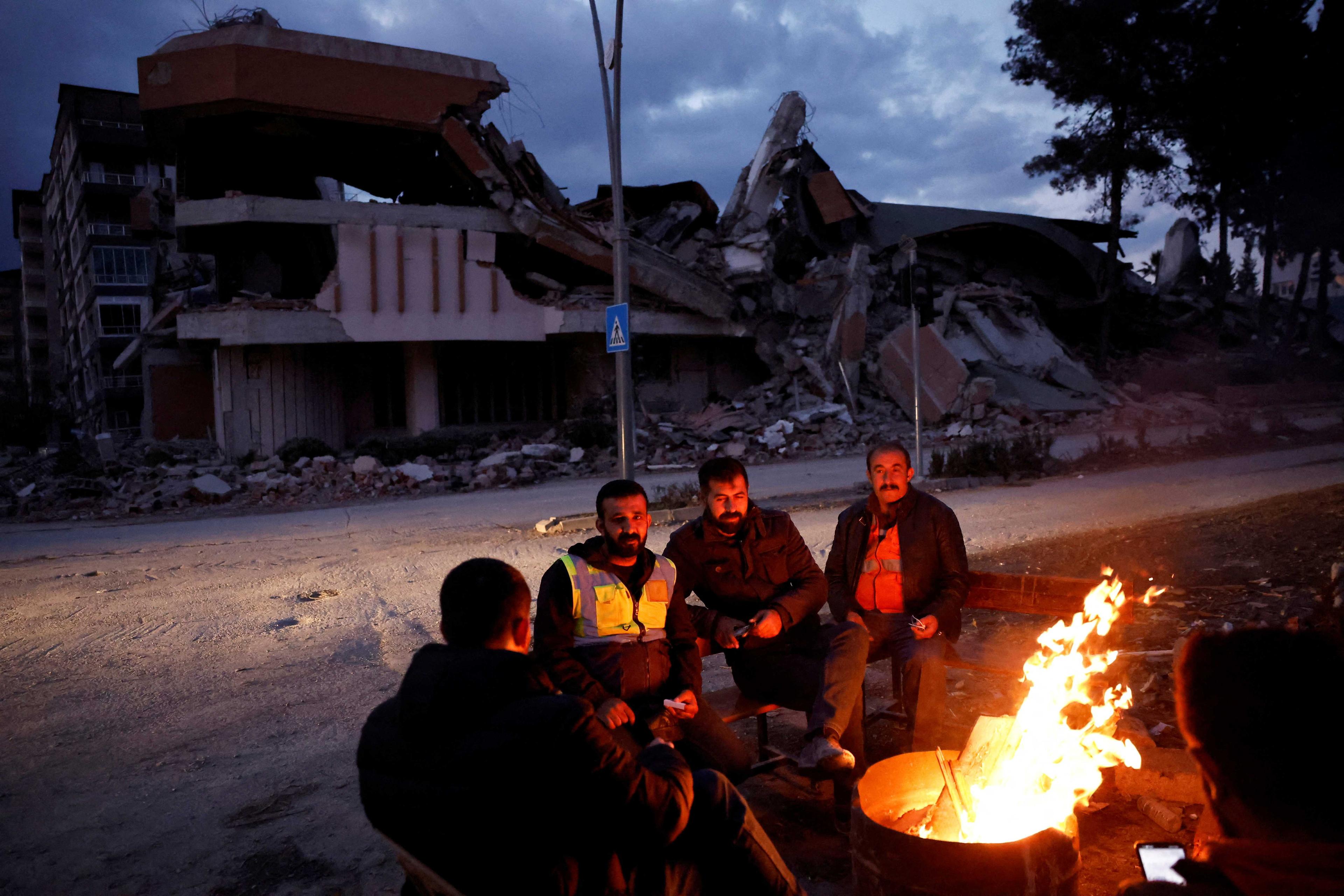 People warm themselves by a fire beside a collapsed building and rubble, in the aftermath of a deadly earthquake, in Antakya, Hatay province, Turkey, Feb 21. Photo: Reuters