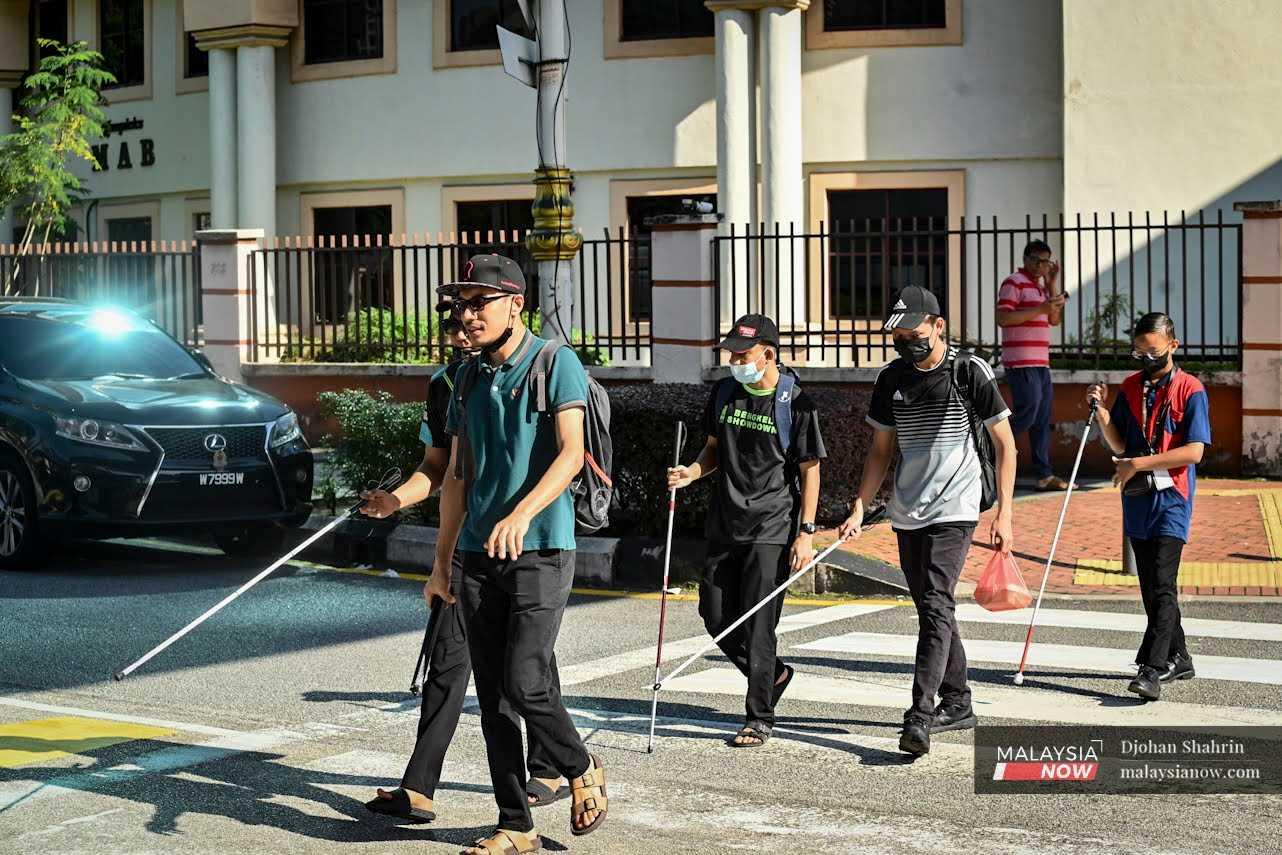 A group of visually impaired individuals cross a road in Brickfields, Kuala Lumpur. 