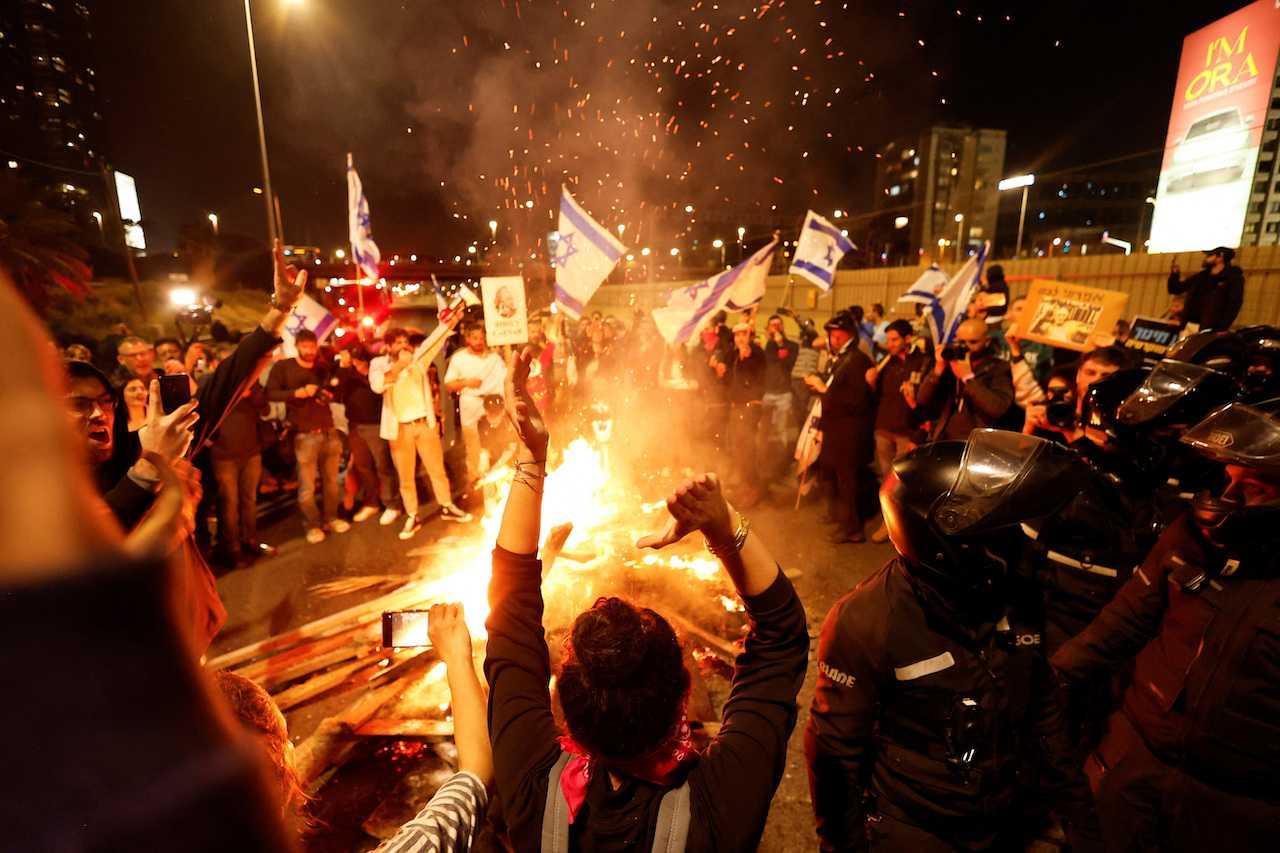 People and police stand next to a bonfire on a road during a protest against Israeli Prime Minister Benjamin Netanyahu's new right-wing coalition and its proposed judicial changes to reduce powers of the Supreme Court in Tel Aviv, Feb 25. Photo: Reuters