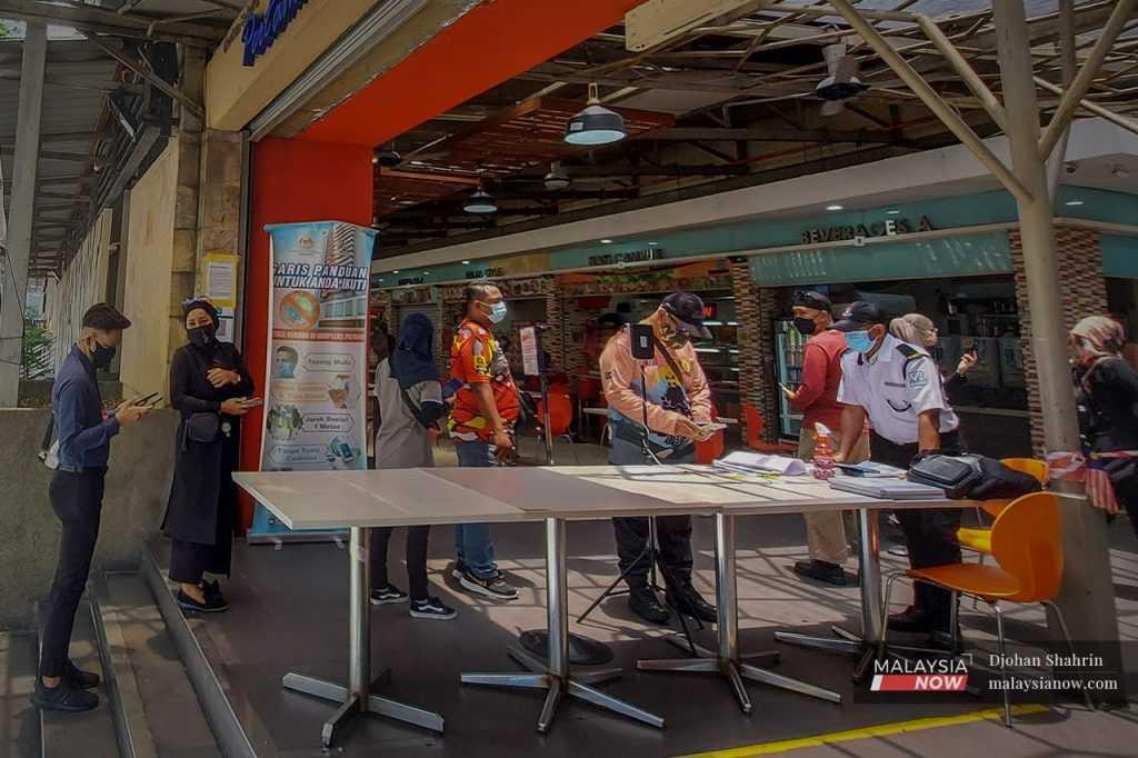 Customers queue to scan the QR code and show their MySejahtera status to the security guard on duty before entering a premise in Kuala Lumpur in this file picture.