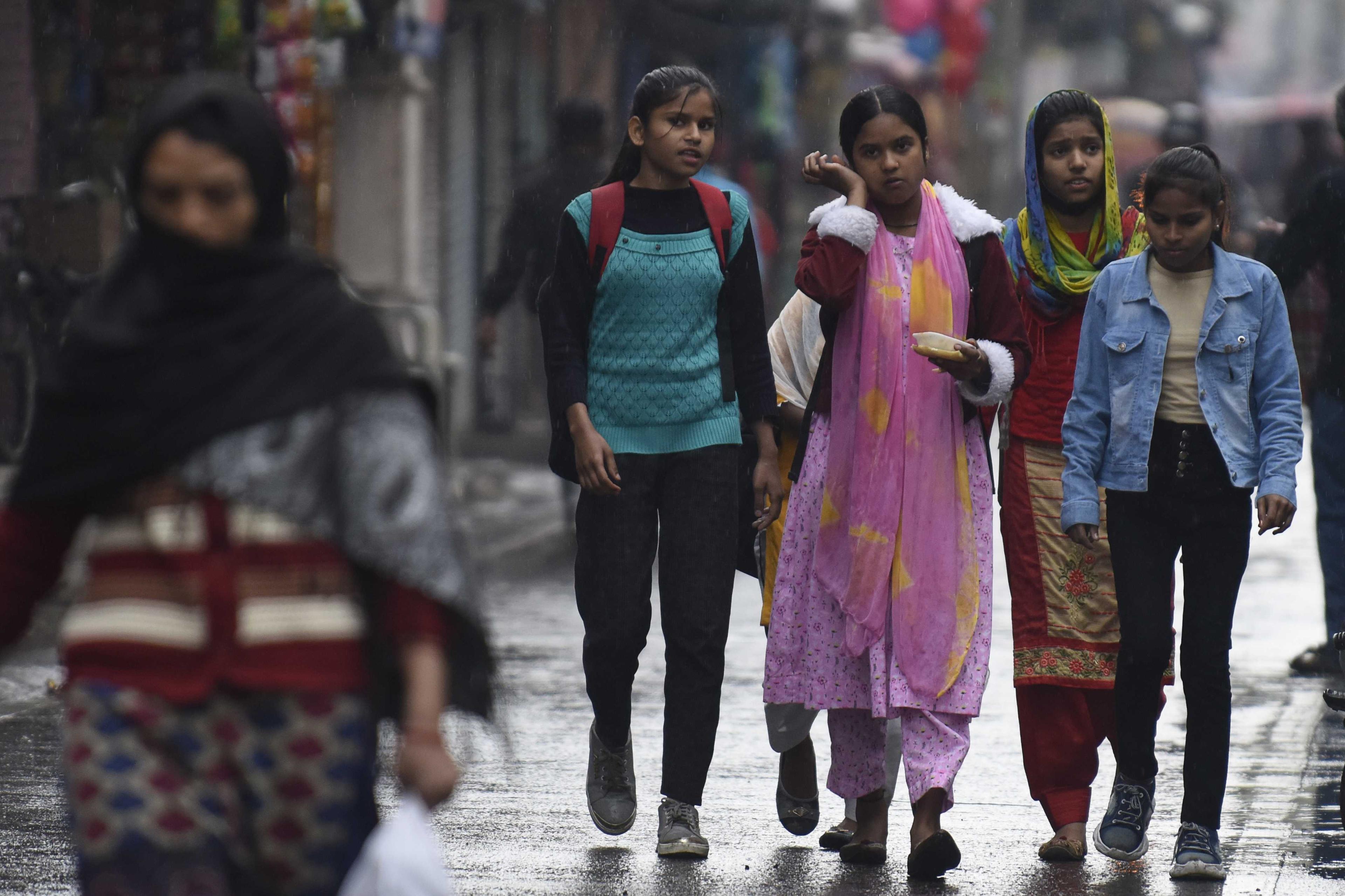 Girls walk along a street during a drizzle in Amritsar on March 3, 2022. Photo: AFP