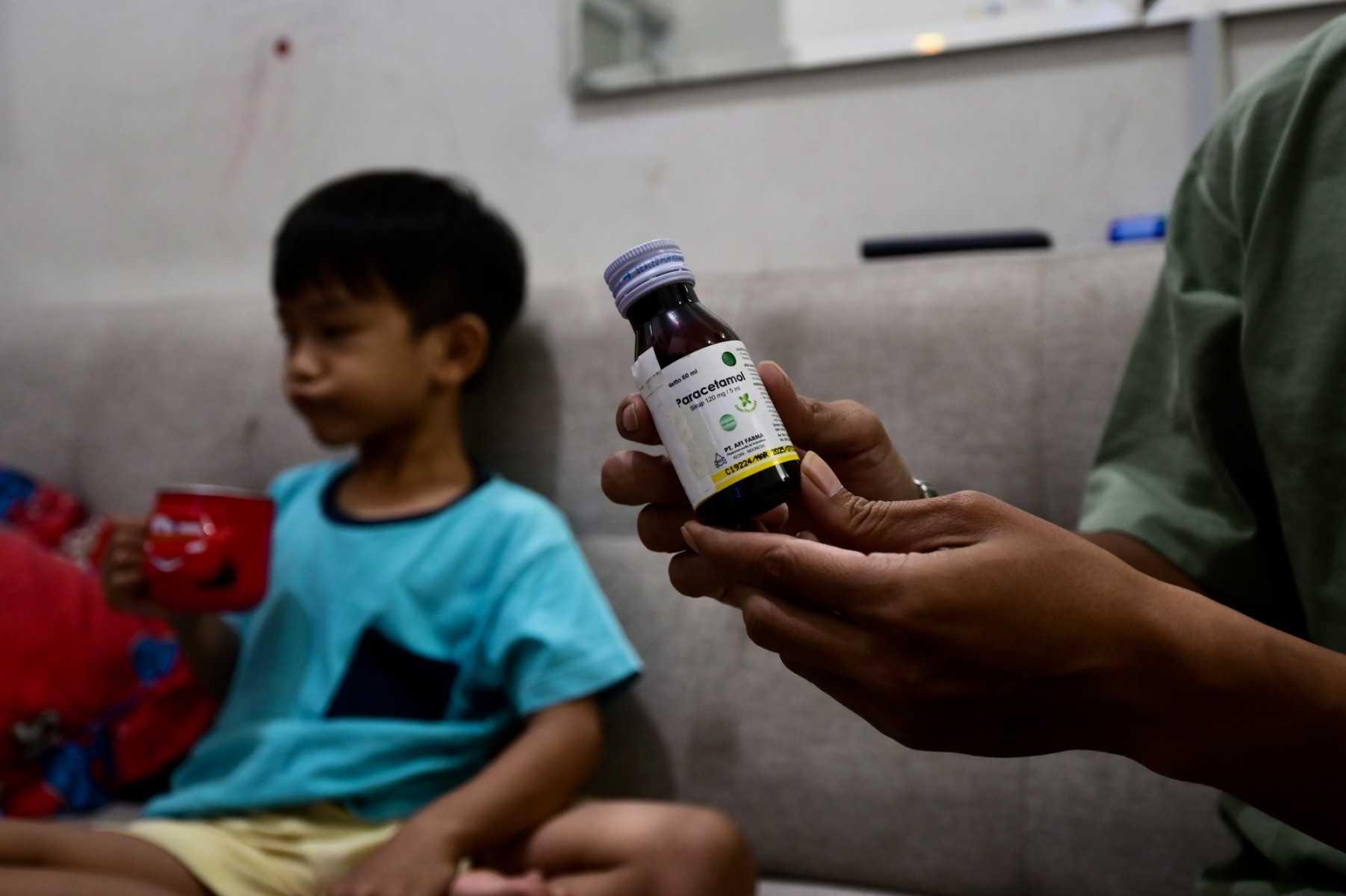 This picture taken on Feb 11, shows Riski Agri (right) displaying a bottle of cough syrup that was consumed by his son Farrazka which caused him kidney problems, at their house in Jakarta. Photo: AFP