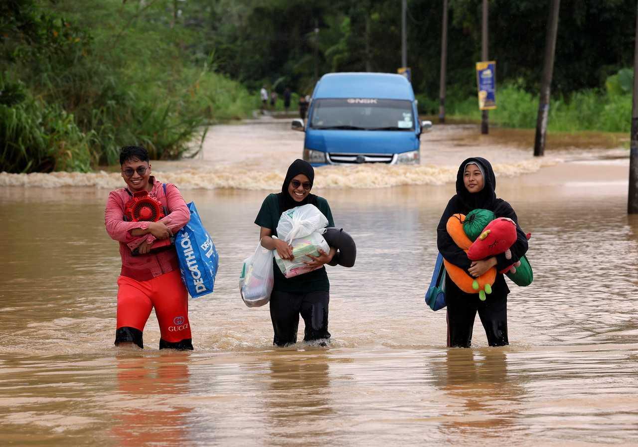 People wade through floodwater as a van makes its way through the flooded road behind them at Kota Tinggi in Johor, March 1. Photo: Bernama
