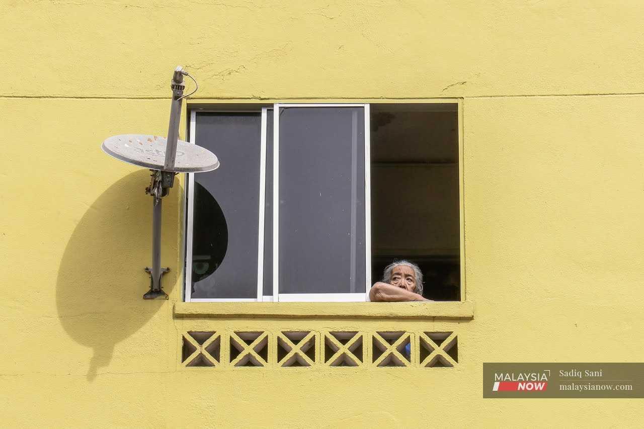 An elderly woman looks out the window at a low-cost housing flat in Kuala Lumpur. 
