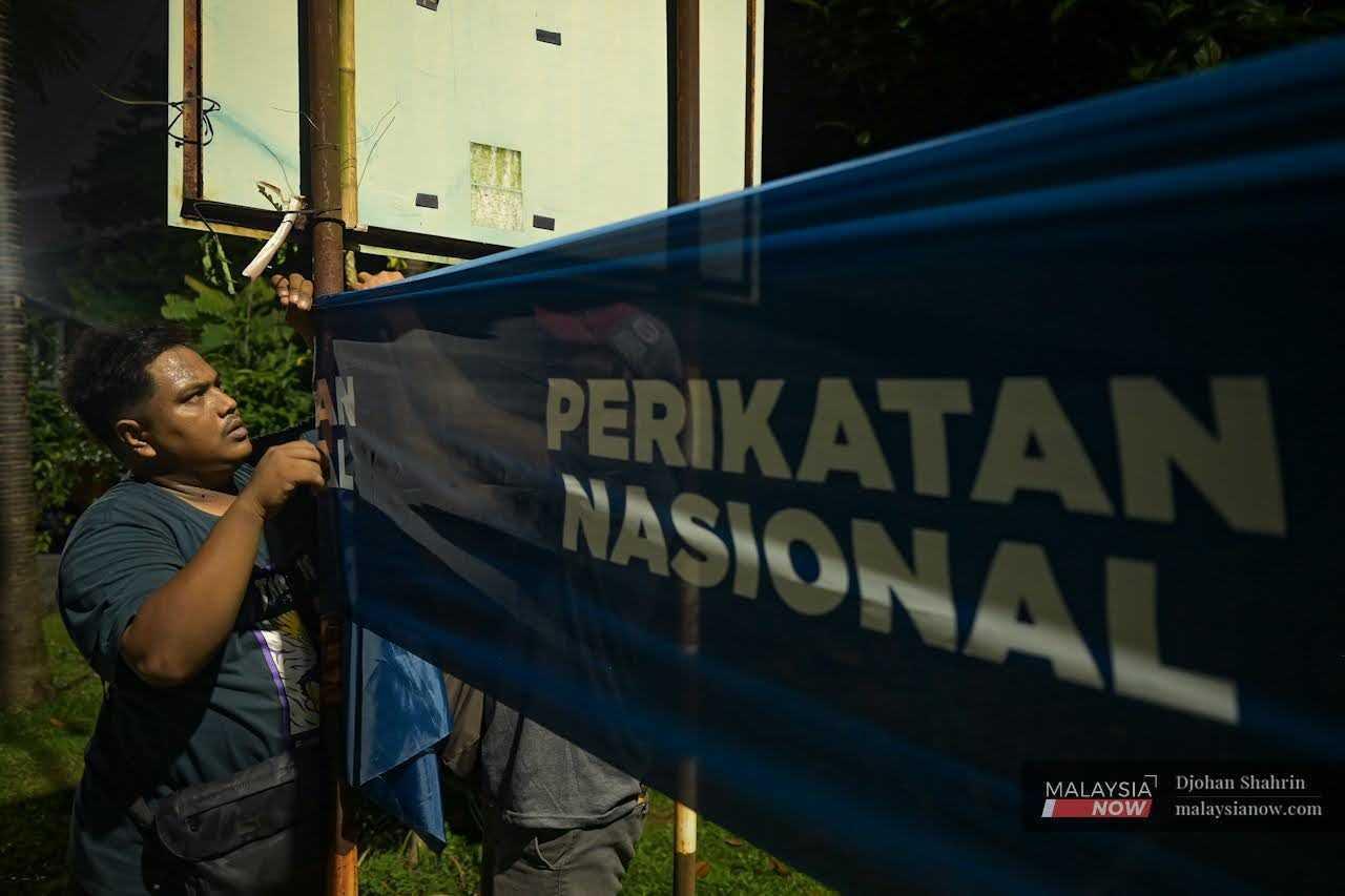 Seorang sukarelawan menggantung bendera Perikatan Nasional sempena kempen Pilihan Raya Umum ke-15 pada 19 November.