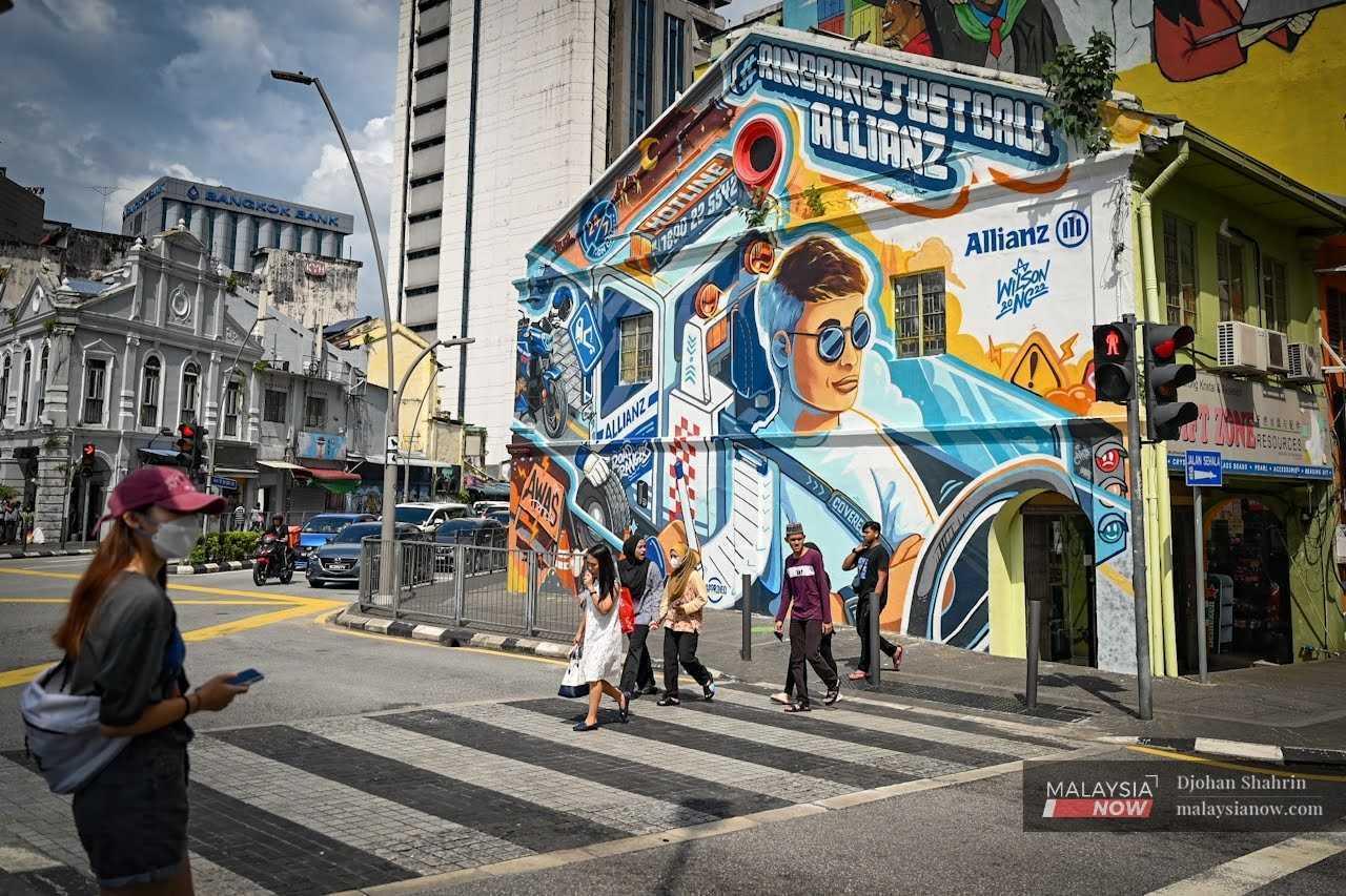 Pedestrians cross a street near a building covered in a mural in the capital city of Kuala Lumpur.
