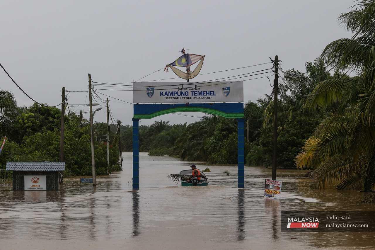 Shaifol Amri navigates his boat under an arch at the main gateway of Kampung Temehel in Yong Peng, Johor, one of many areas that have been inundated for days.