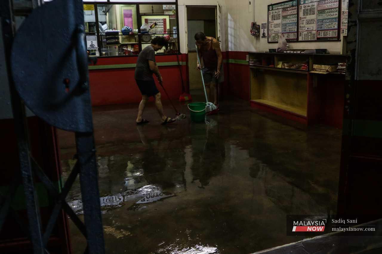 A couple in Kota Tinggi, Johor, clean their shop lot after the flood water begins to subside. 