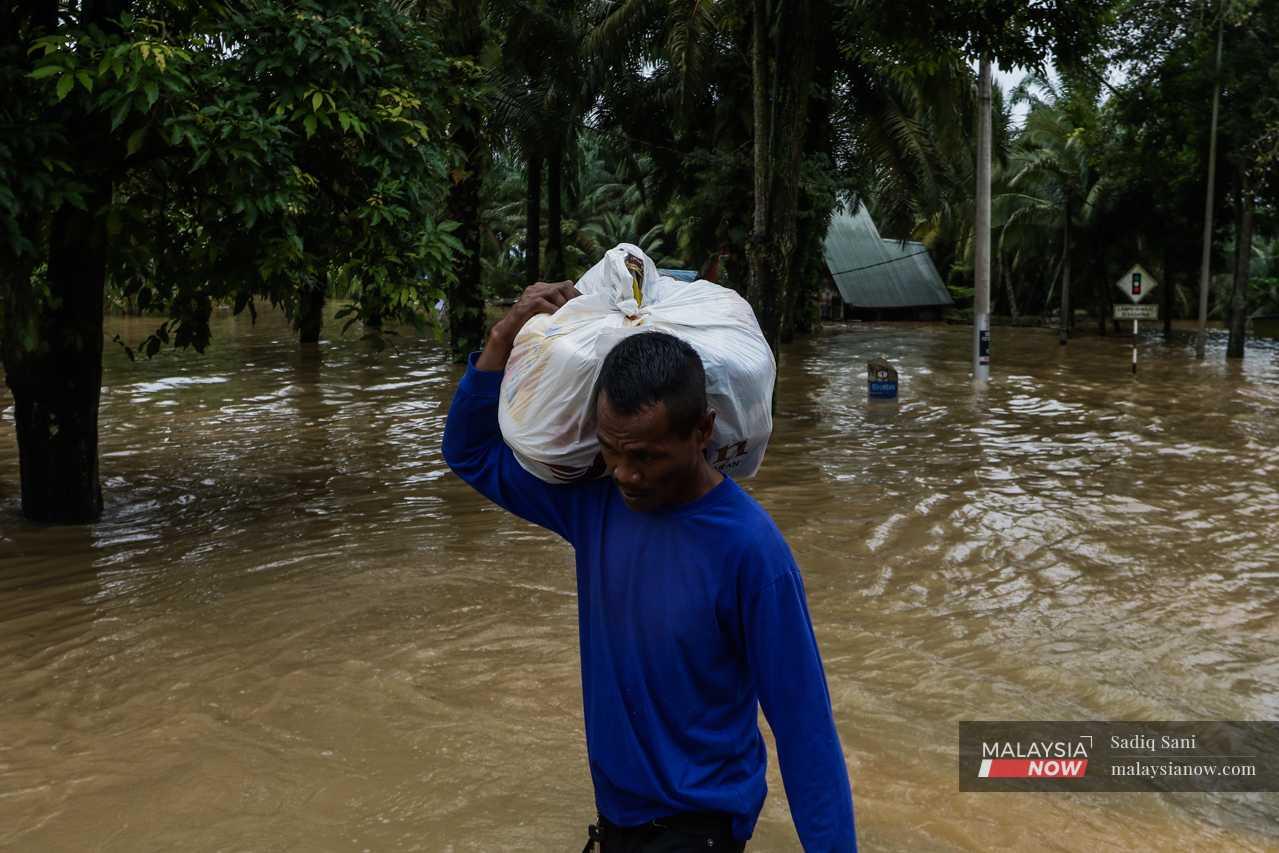 Seorang lelaki mengangkut beg plastik berisi barangan di bahu selepas rumahnya dinaiki air di Kampung Temehel di Yong Peng, Johor.