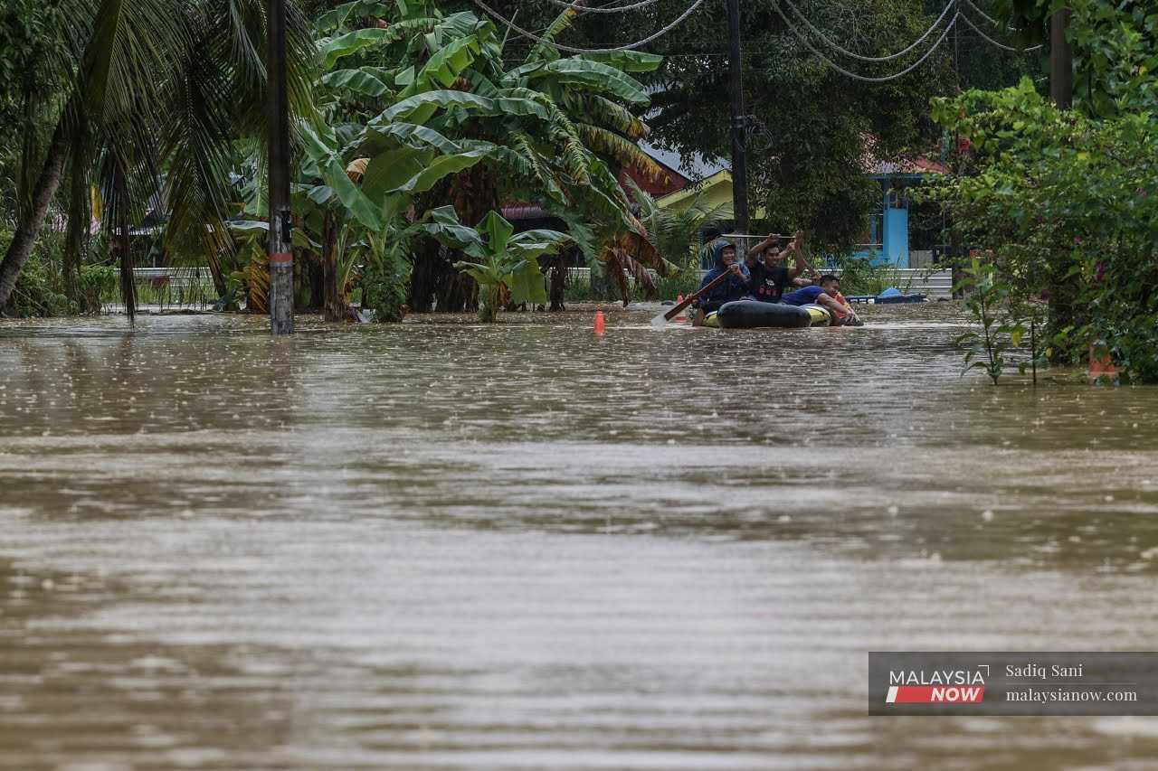 Locals paddle through flood water in an inflatable boat in Kampung Melayu, Yong Peng in Johor.