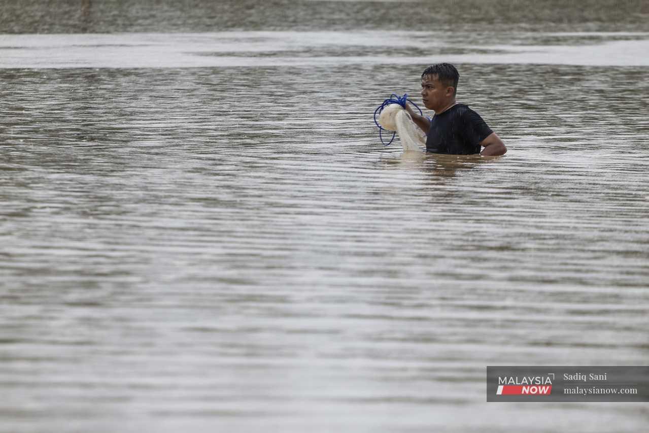 A man wades with a fishing net through chest-deep water in Yong Peng, Johor. 