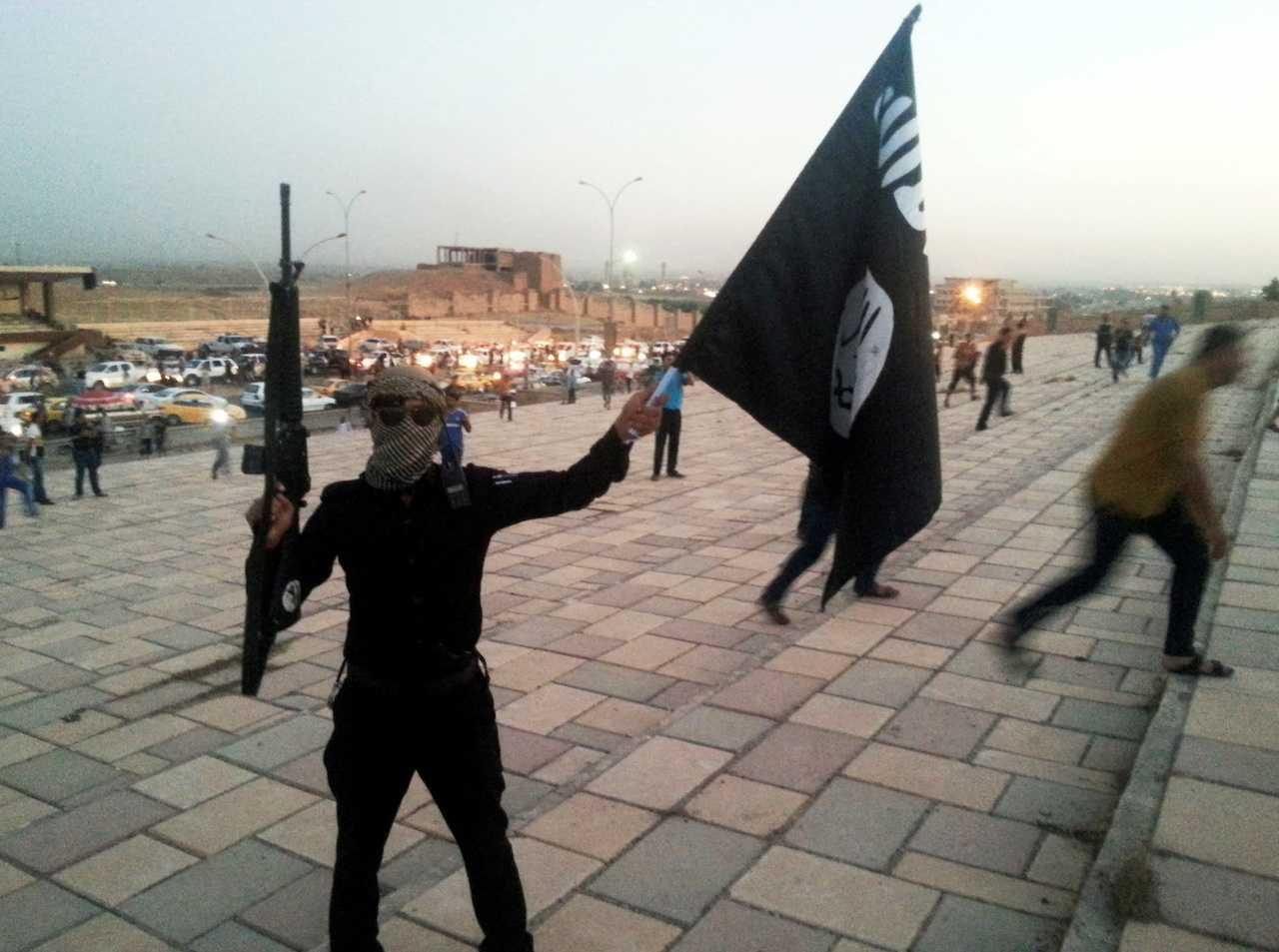 An Islamic State fighter holds a flag and a weapon on a street in the city of Mosul, June 23, 2014. Photo: Reuters