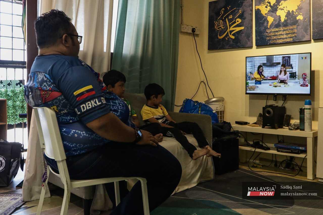 In one of the small units, Zaimi, the president of the residents' association, watches a cooking show with his two sons. 