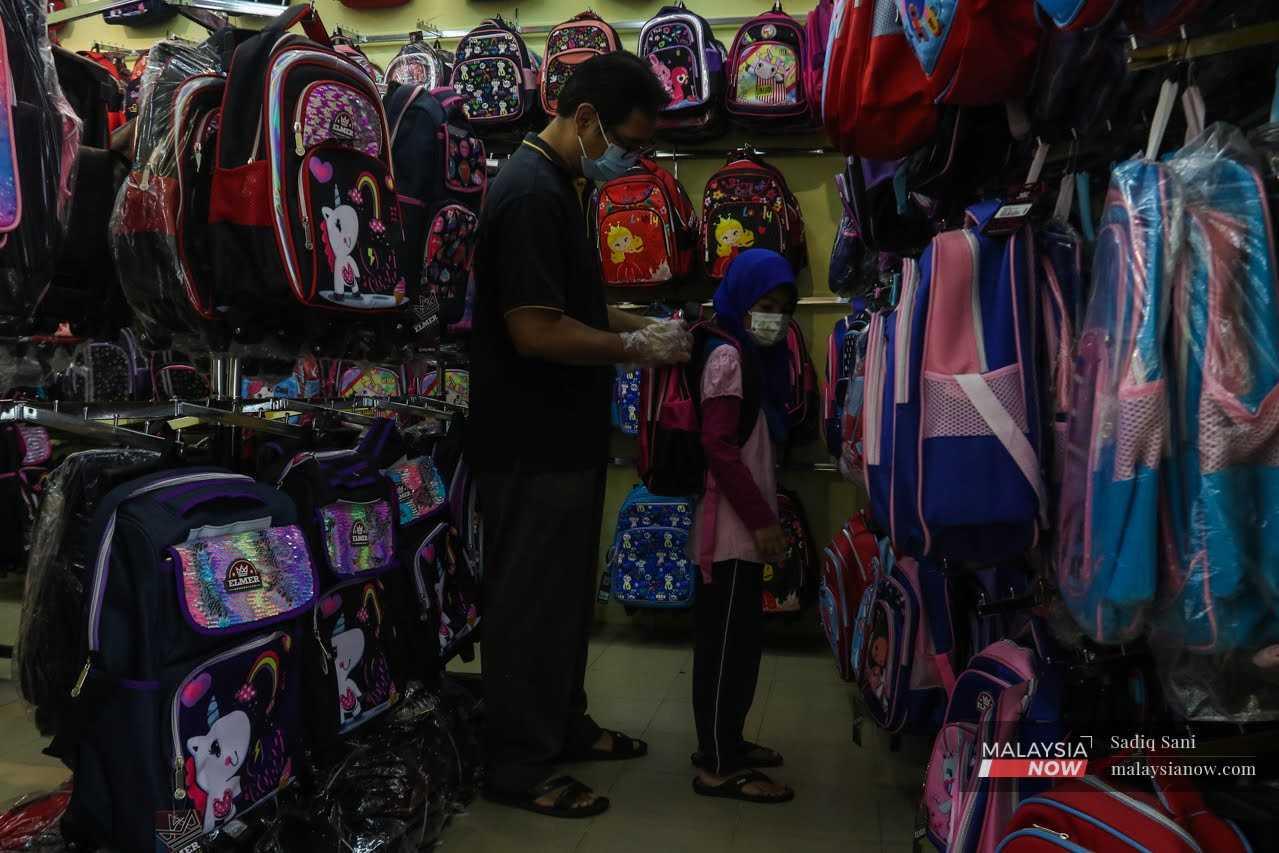 Seorang bapa membantu anak perempuannya memilih beg galas ketika sedang membuat persiapan sesi persekolahan yang bermula hari ini di Lembah Klang, 18 Mac.