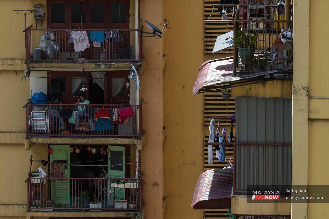 A woman speaks on the phone at her balcony, which does double duty as a laundry and storage area. 