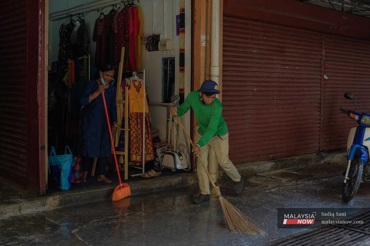 A contract cleaner helps wash the floor in front of a sari shop at the flats.