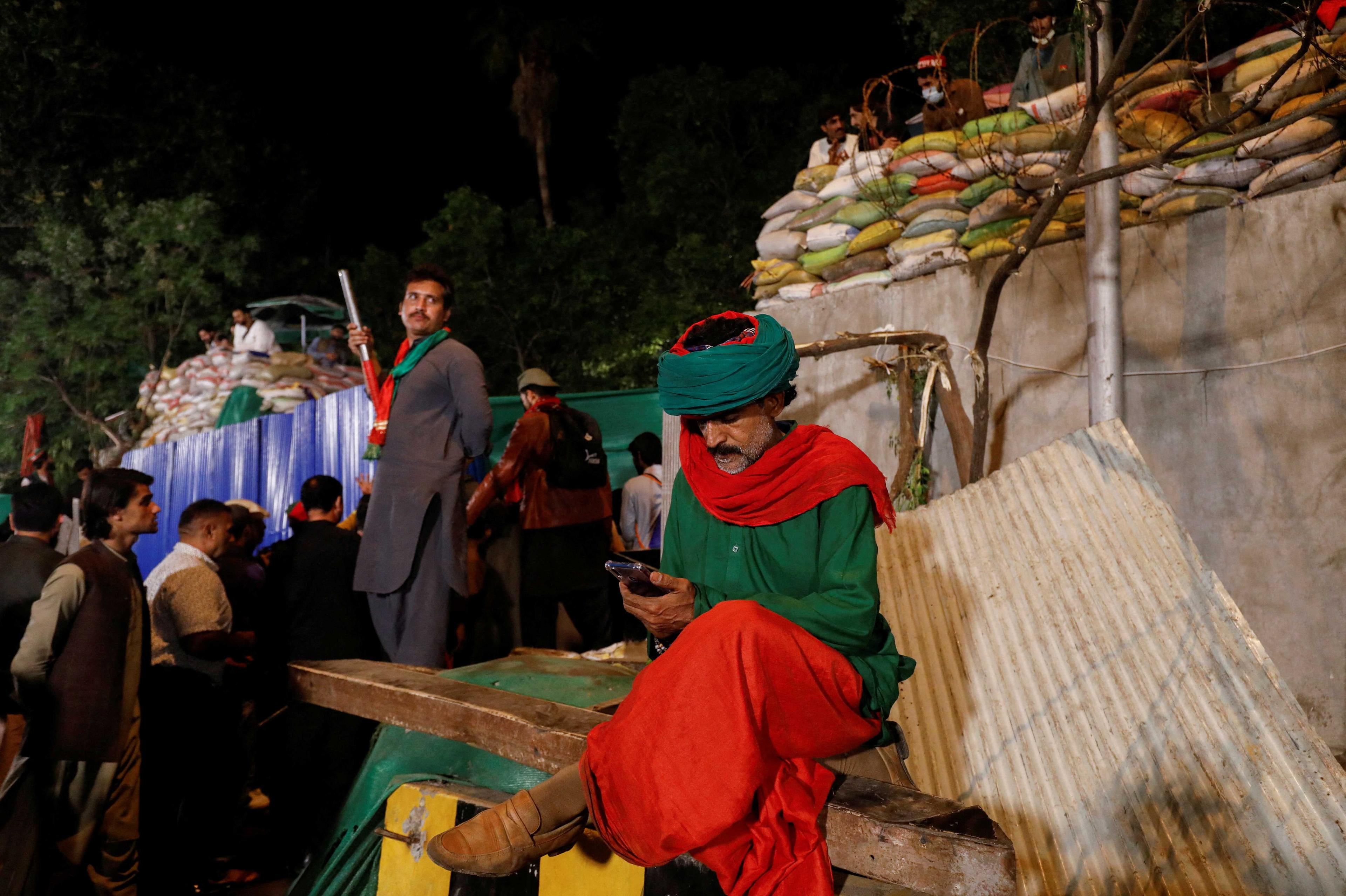 A supporter of former Pakistani Prime Minister Imran Khan sits outside the entrance of Khan's house, wearing attires with the colours of the party's flag, days after clashing with police, in Lahore, Pakistan March 20. Photo: Reuters