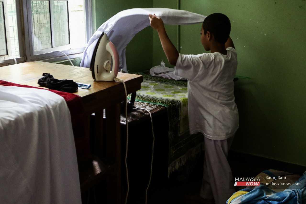 In another room, a boy spreads out a shirt as he prepares to iron it ahead of the Friday prayers. 