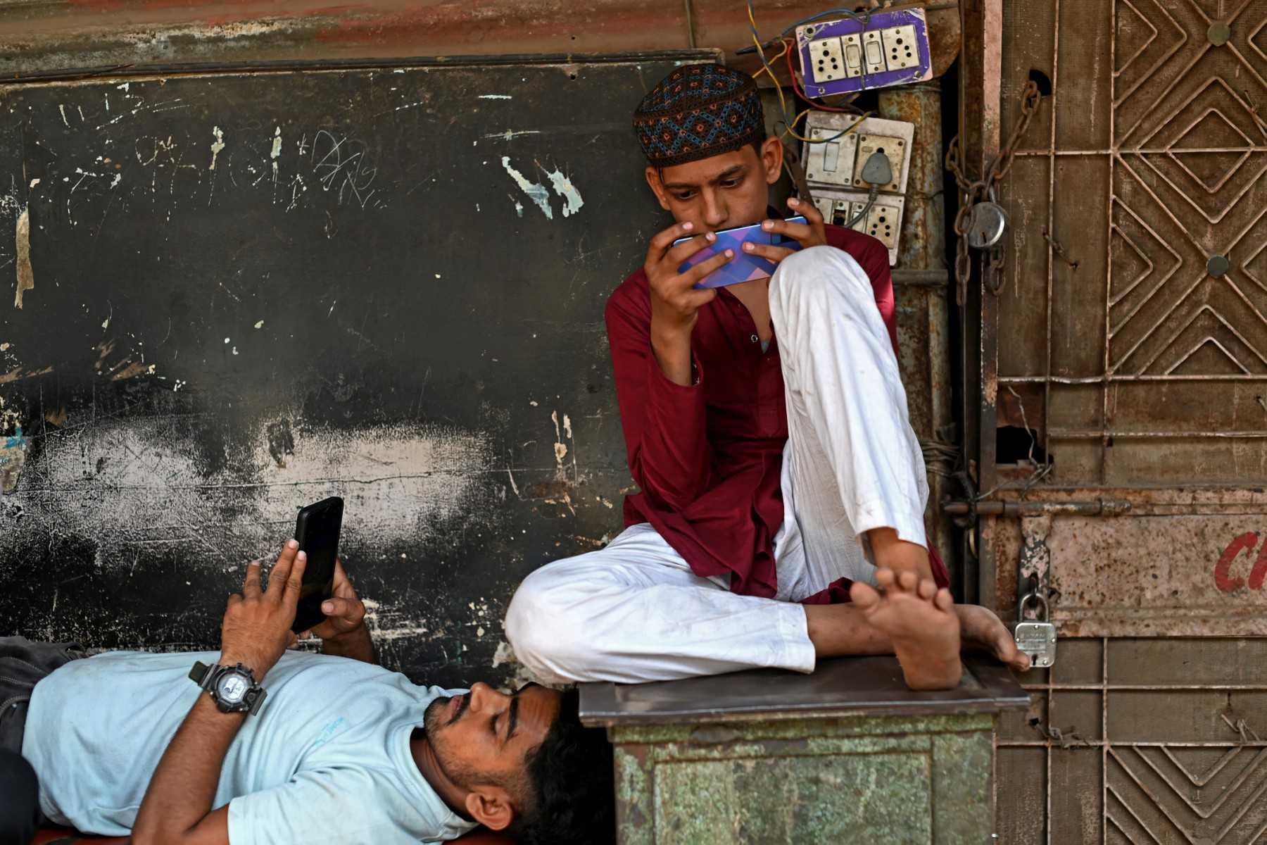 Local residents use their mobile phones while sitting in an alley in New Delhi on May 4, 2022. Photo: AFP