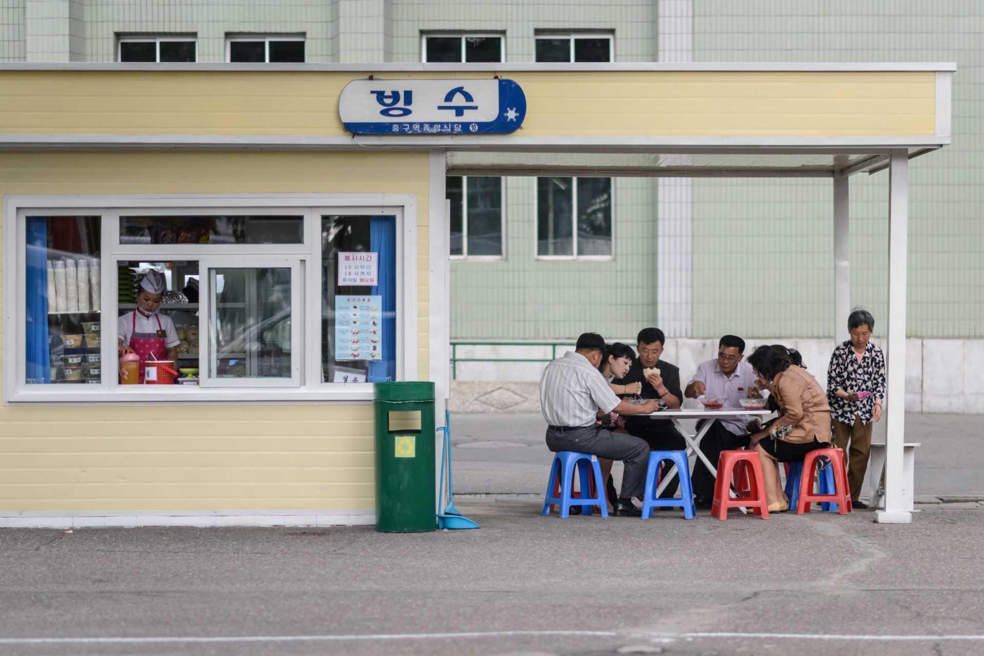 In a photo taken on June 21, 2019 a group of diners sit around a table beside a food and snack stall on a street in Pyongyang. Photo: AFP 