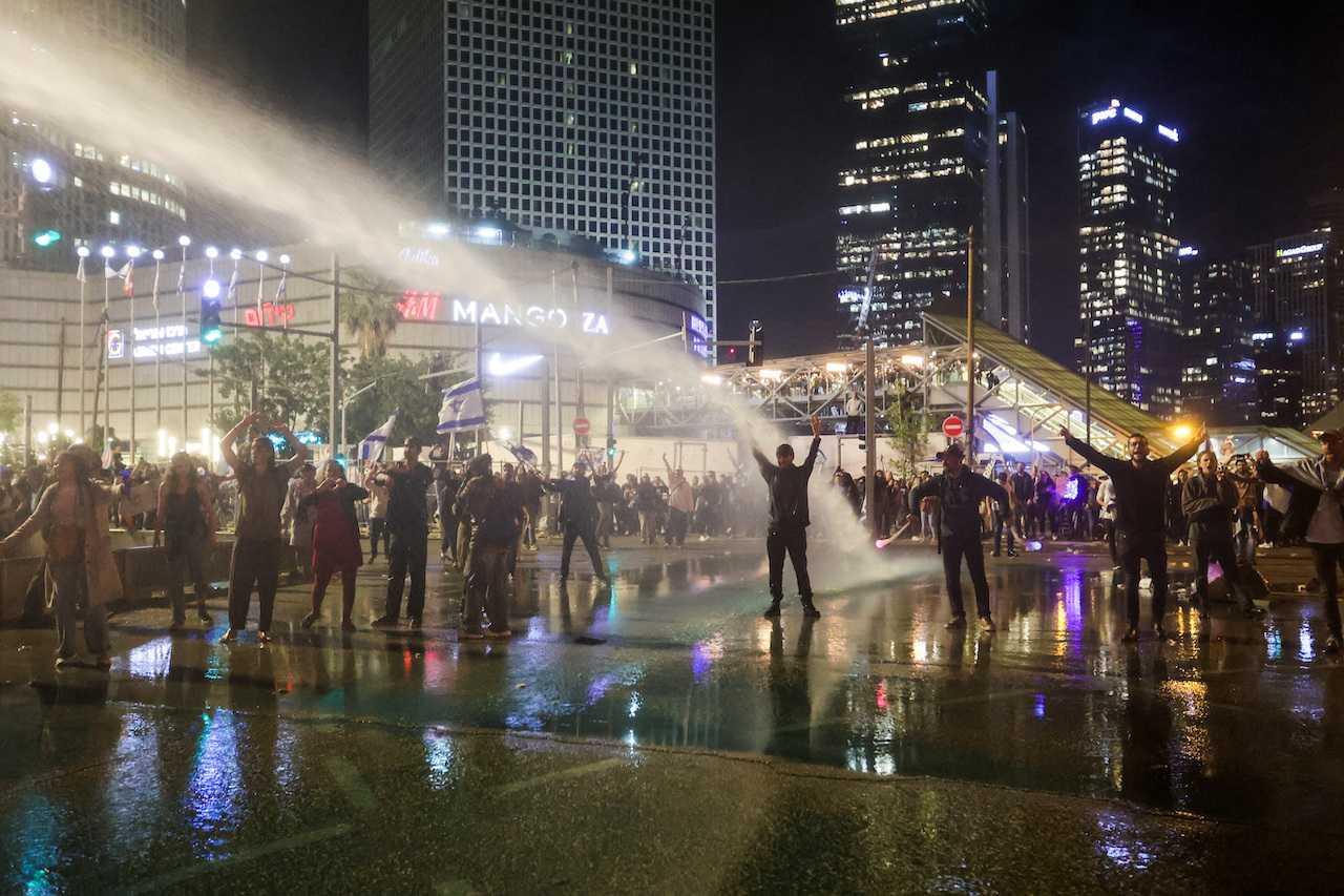 Israeli protesters stand with their arms up as a water cannon is used to disperse the people attending a demonstration against Prime Minister Benjamin Netanyahu and his nationalist coalition government's plan for judicial overhaul, in Tel Aviv, March 27. Photo: Reuters