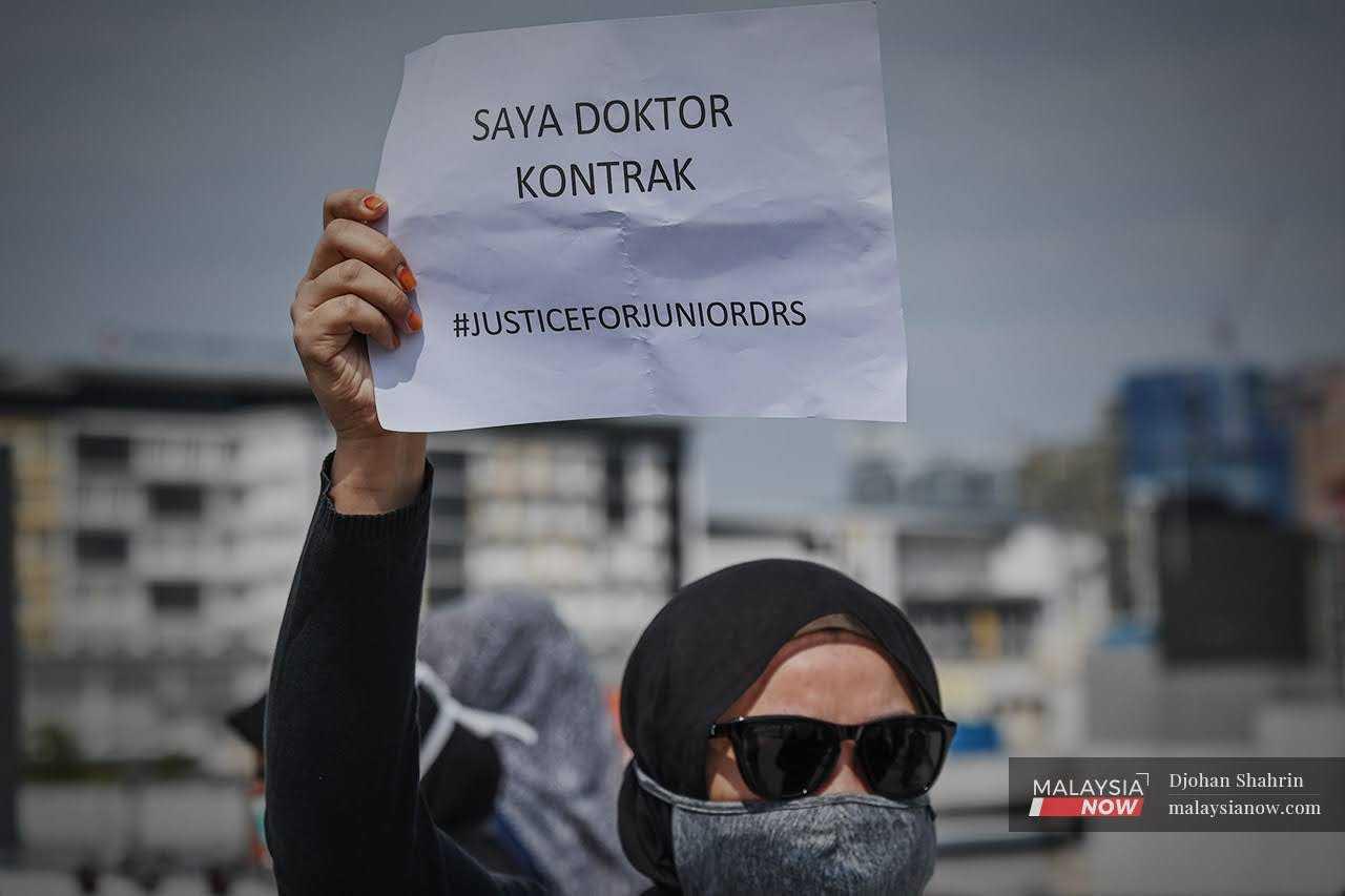 A contract doctor holds up a placard during a peaceful walkout at Hospital Kuala Lumpur on July 26, 2021.