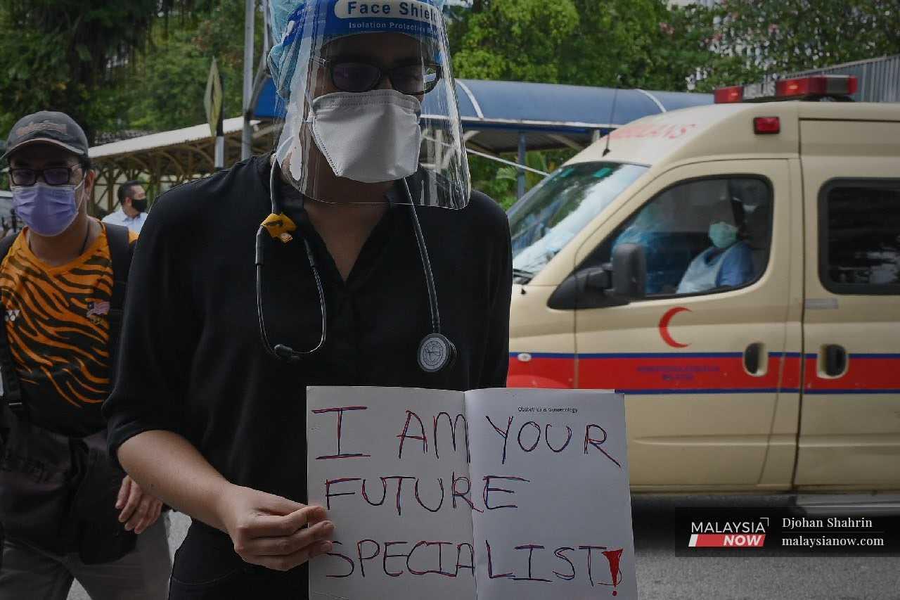 A contract doctor holds up a placard during a peaceful walkout at Hospital Kuala Lumpur on July 26, 2021.