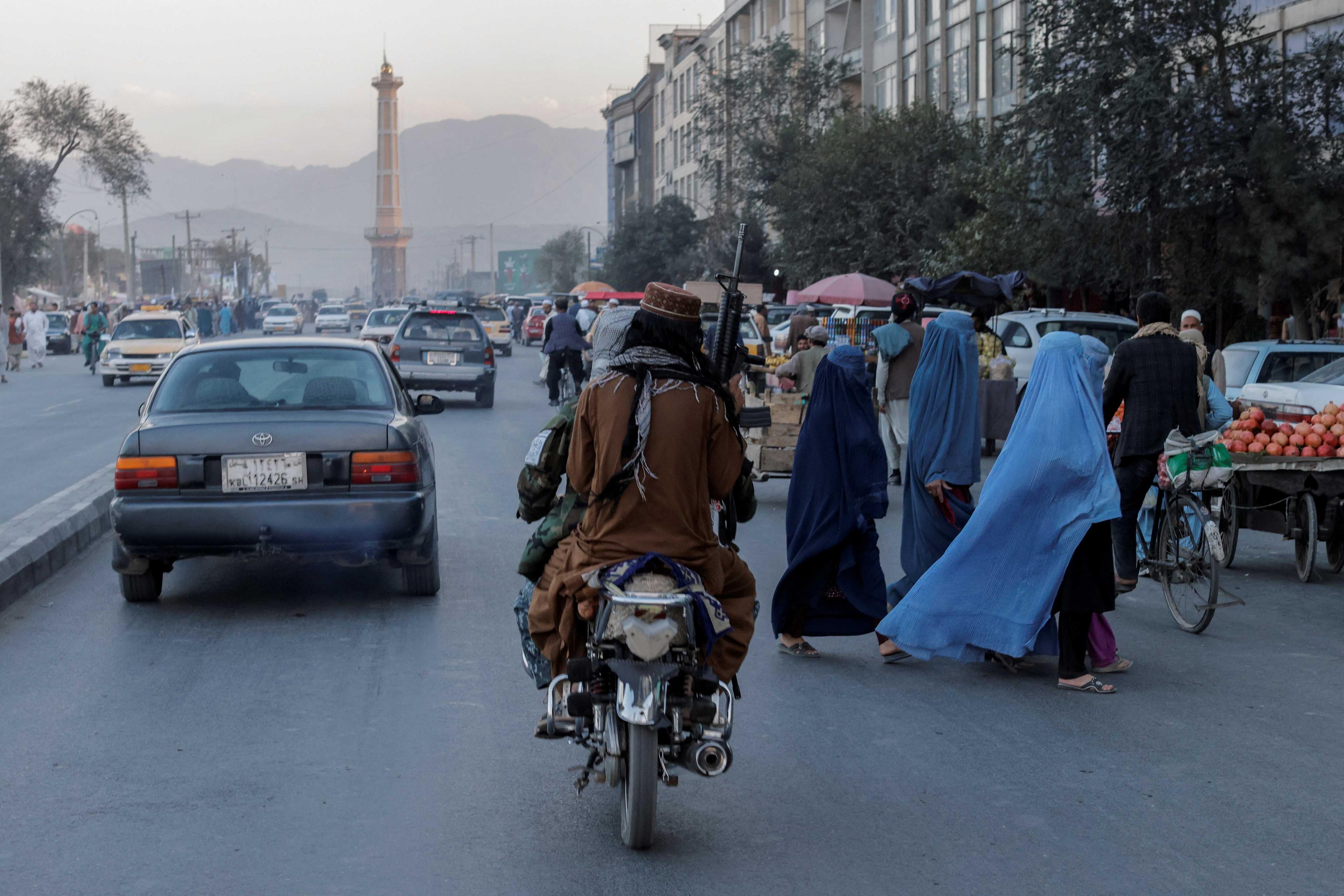 A group of women wearing burqas crosses the street as members of the Taliban drive past in Kabul, Afghanistan Oct 9, 2021. Photo: Reuters