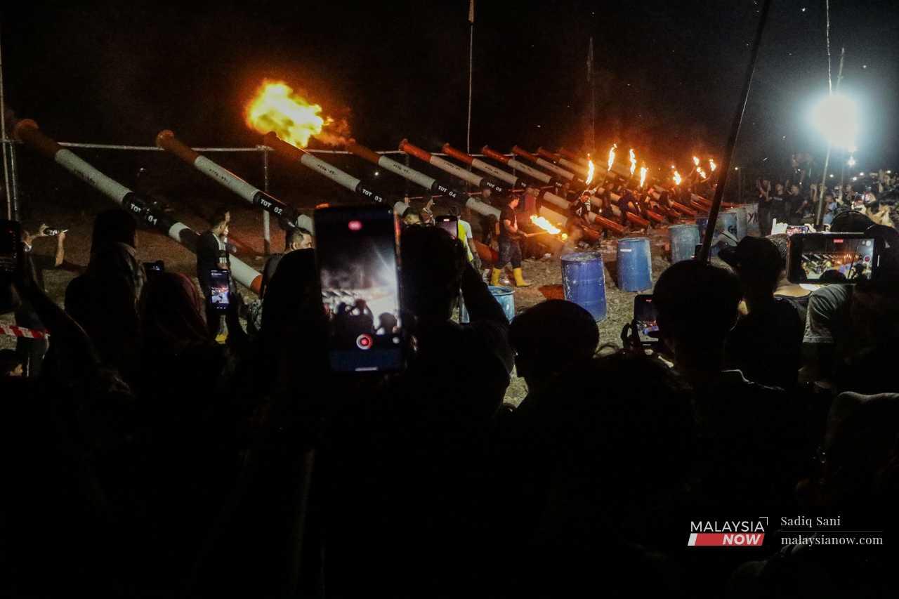 Visitors stand safely behind the line of fire, with camera phones in hand.