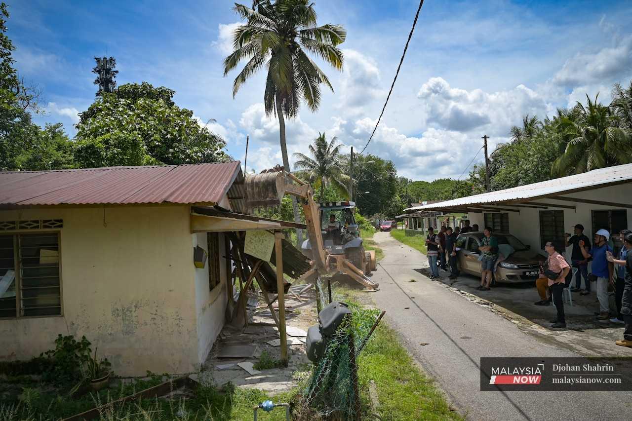 Penduduk kampung melihat jentolak mula merobohkan salah satu rumah. 