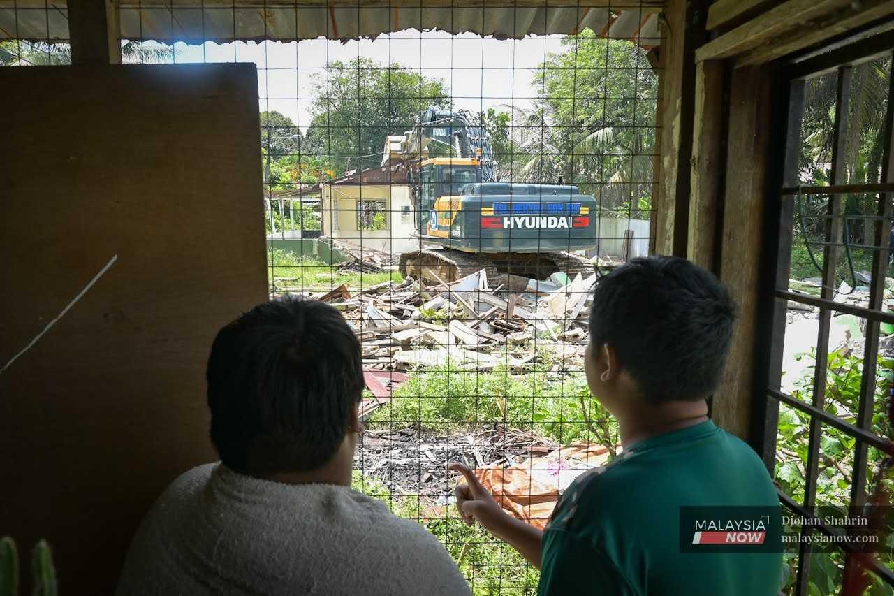 Dua penduduk melihat jentolak merobohkan rumah secara berperingkat sewaktu proses pengambilan tanah Kampung Koskan Tambahan dari penduduk kampung di Serendah, Rawang, 3 Mei.