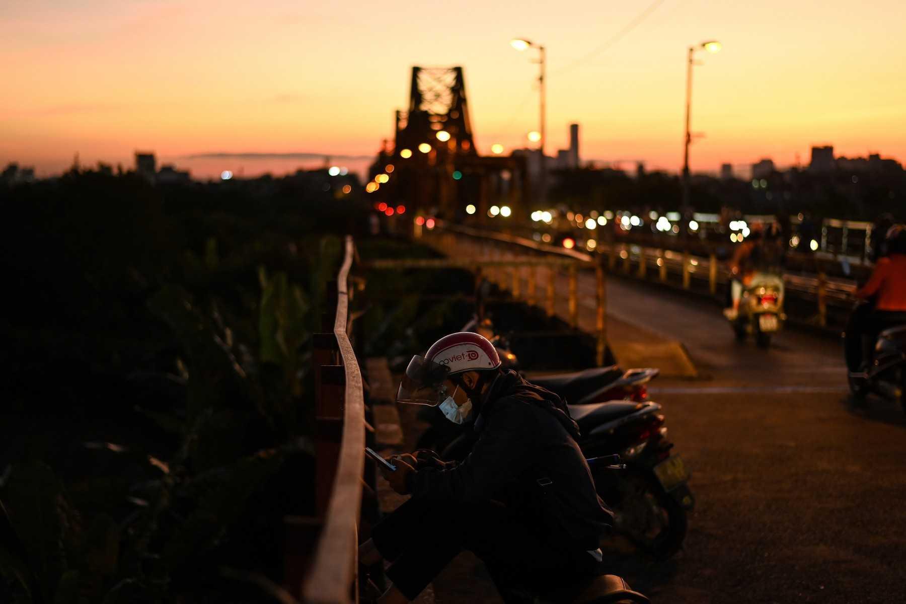 A man checks his smartphone while waiting on the century-old Long Bien bridge at dusk in Hanoi on Oct 12, 2021. Photo: AFP 