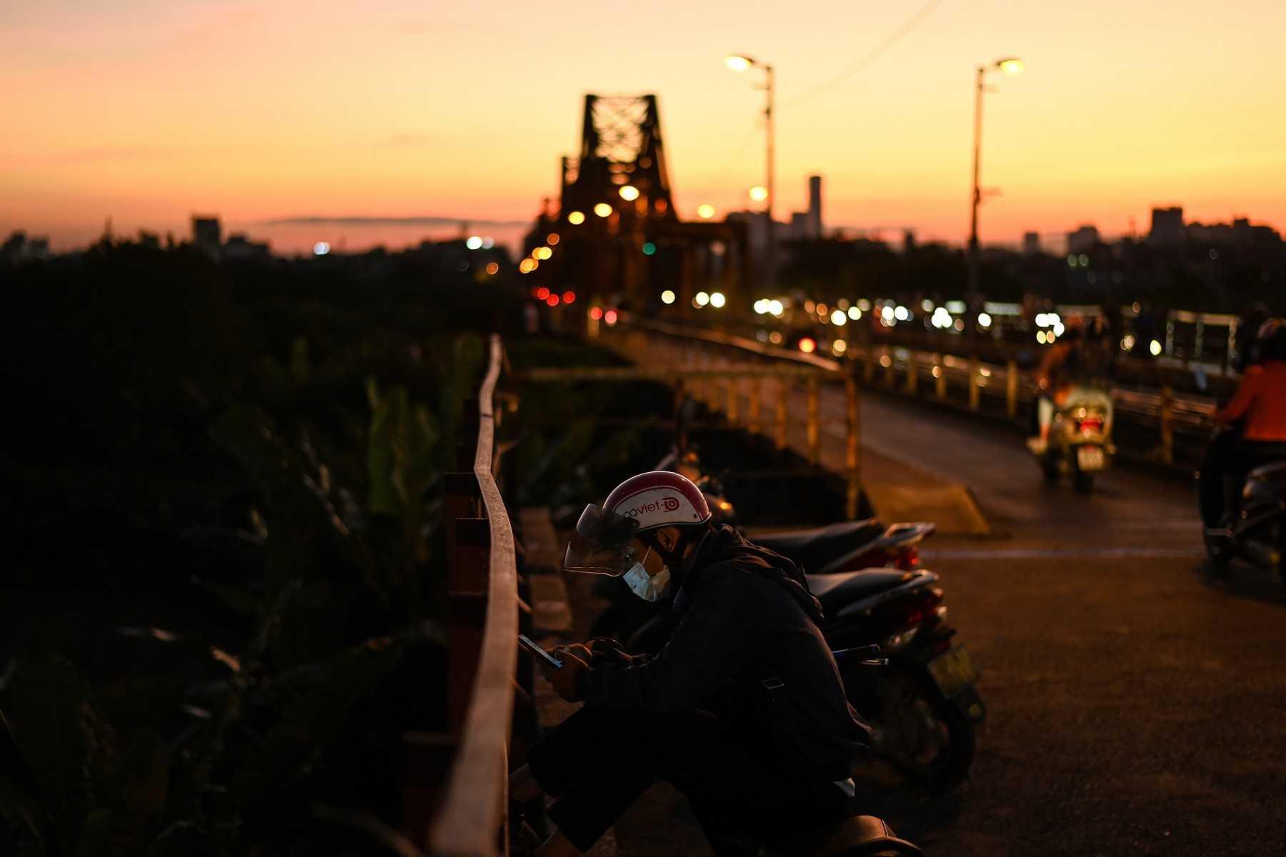A man checks his smartphone while waiting on the century-old Long Bien bridge at dusk in Hanoi on Oct 12, 2021. Photo: AFP