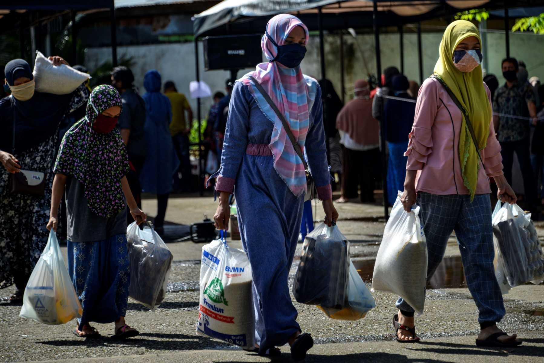 Wanita memakai pelitup muka membawa barang-barang runcit yang dibeli di pusat stok makanan kerajaan di Banda Aceh pada 14 Mei 2020. Gambar: AFP