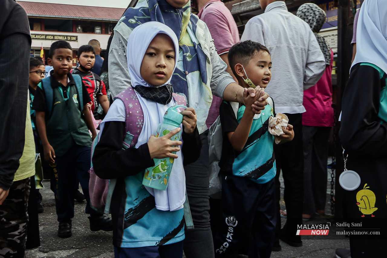 Murid-murid sekolah memegang botol air sewaktu mereka hadir ke sekolah dengan berpakaian sukan semasa musim panas.