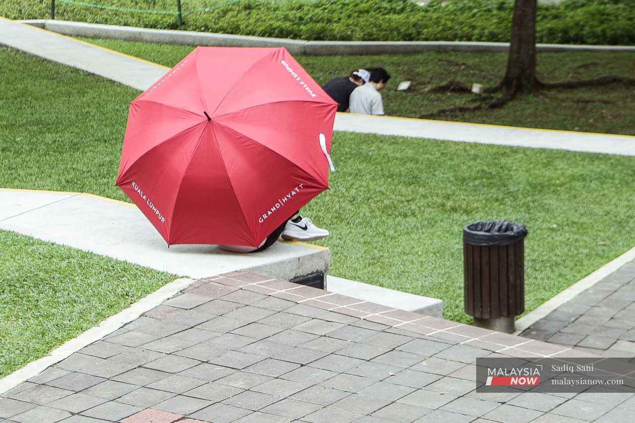 A person hides under an umbrella as the sun pours down overhead.