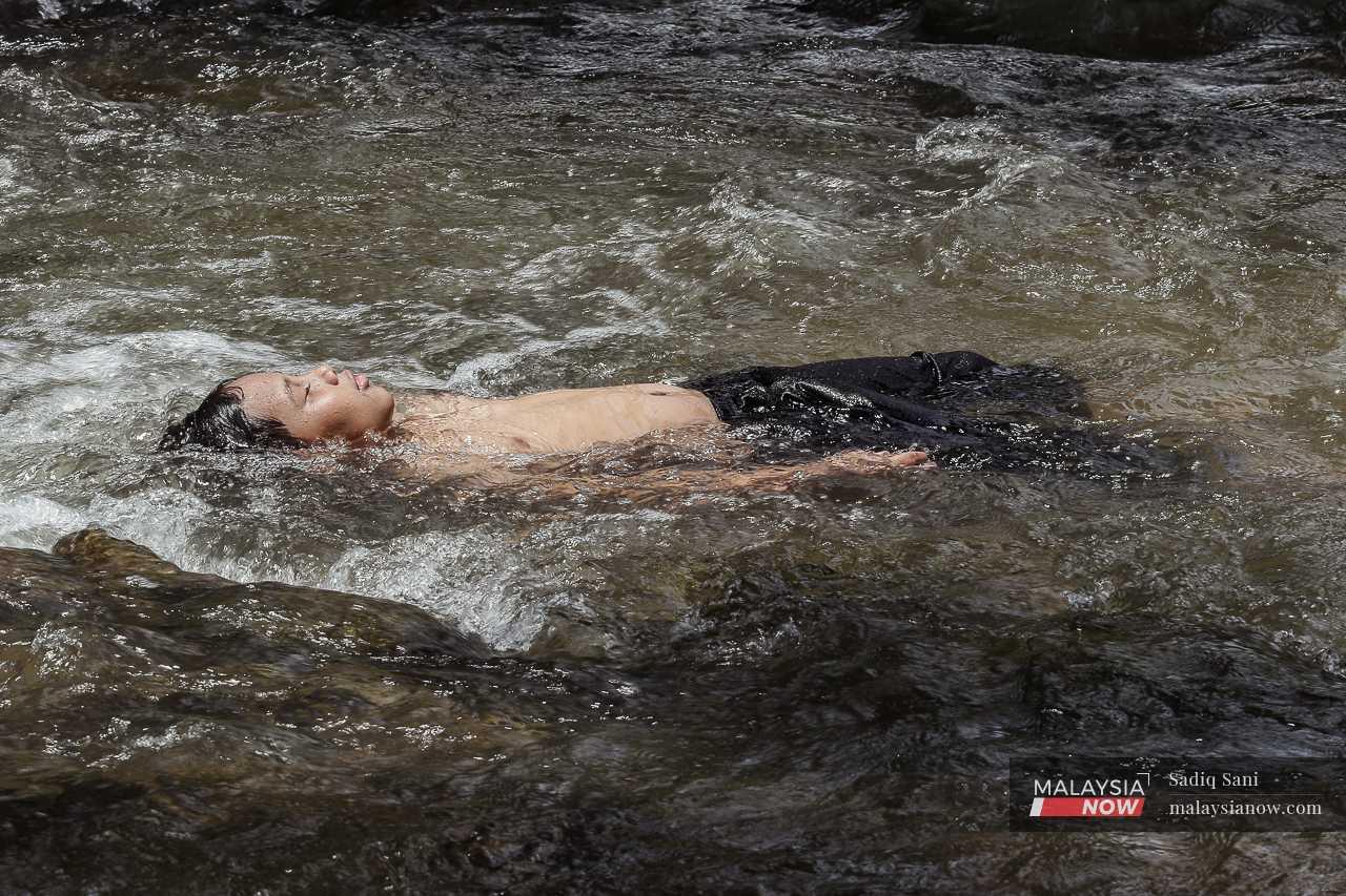 A boy floats in the water, enjoying the coolness of the stream. 