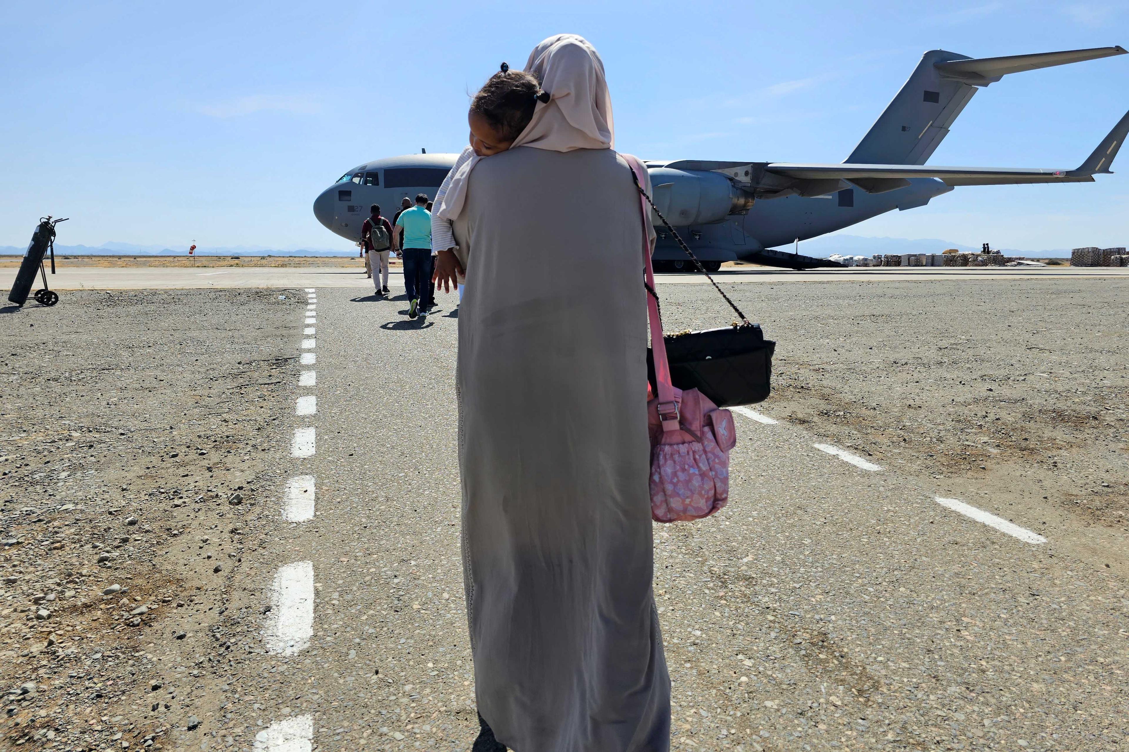 An evacuee holding a sleeping toddler walks toward an Abu Dhabi-bound Emirati plane at Port Sudan airport on May 10, as violence between two rival Sudanese generals continues. Photo: AFP