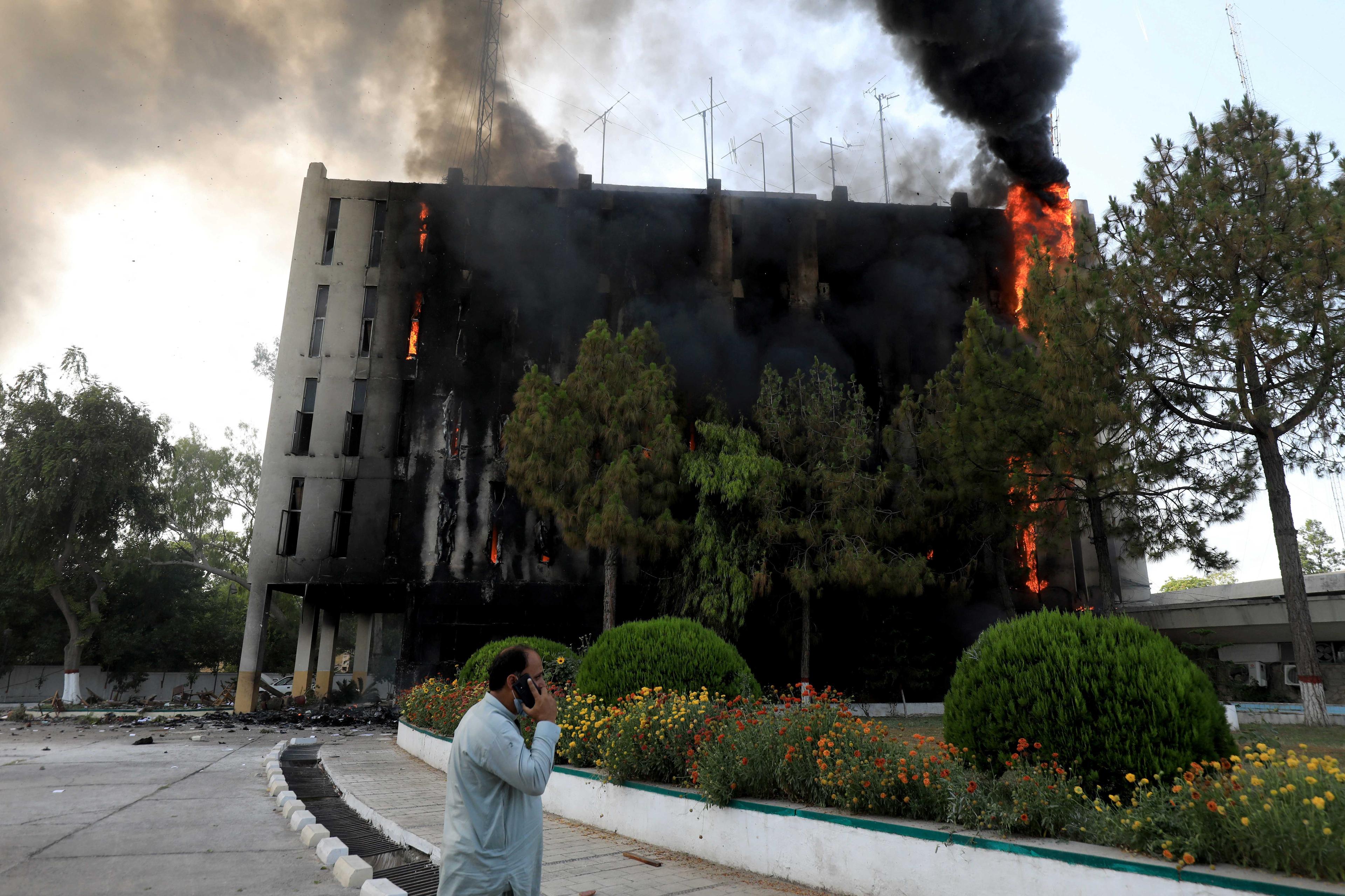 A man speaks on his mobile as fire and smoke billow from a Radio Pakistan building after it was set afire by the supporters of Pakistan's former Prime Minister Imran Khan during a protest against his arrest, in Peshawar, Pakistan, May 10. Photo: Reuters