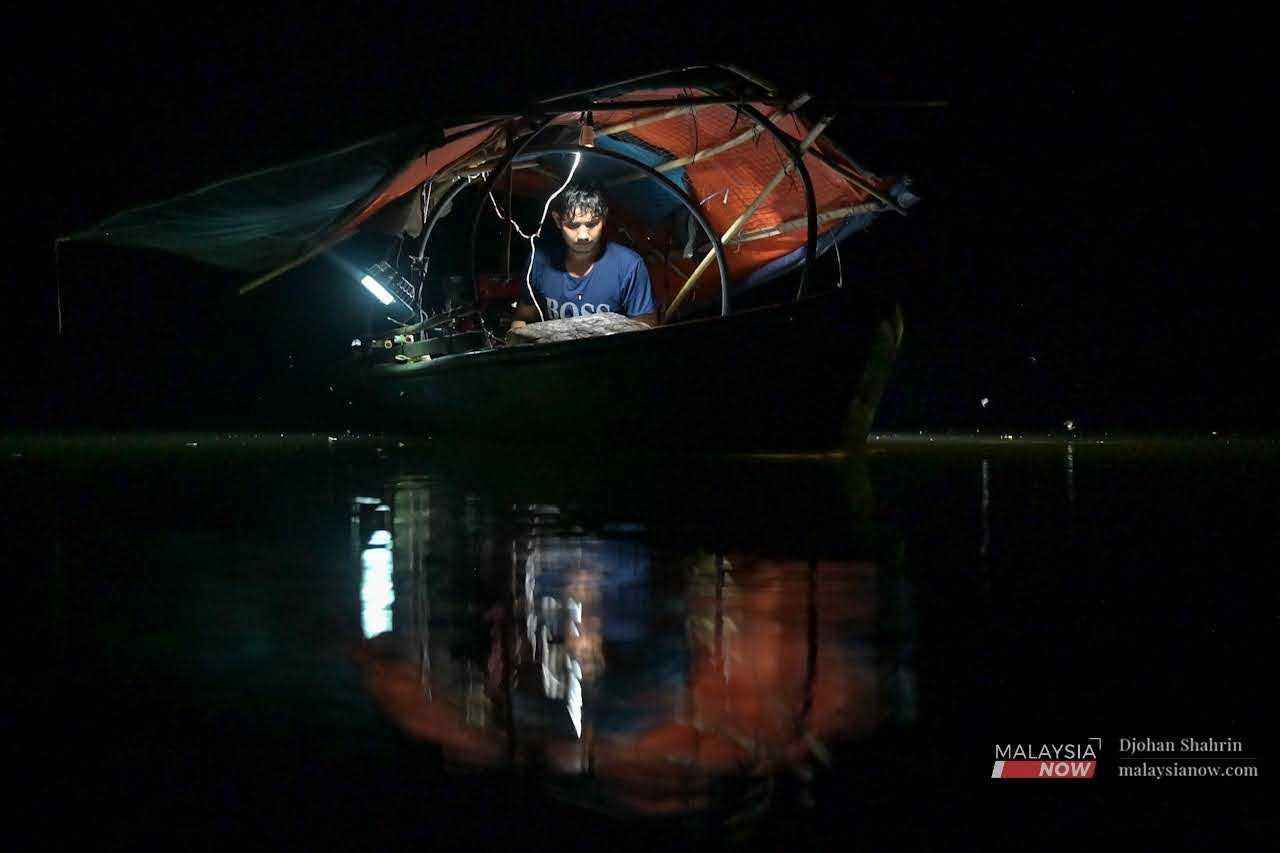 Nelayan darat, Wan Ikmal Izham Wan Yusof, 26, memasang wayar-wayar lampu bot untuk di suluh ke permukaan air bagi menarik perhatian ikan renik di Sungai Bersia, Hulu Perak, 11 Mei.