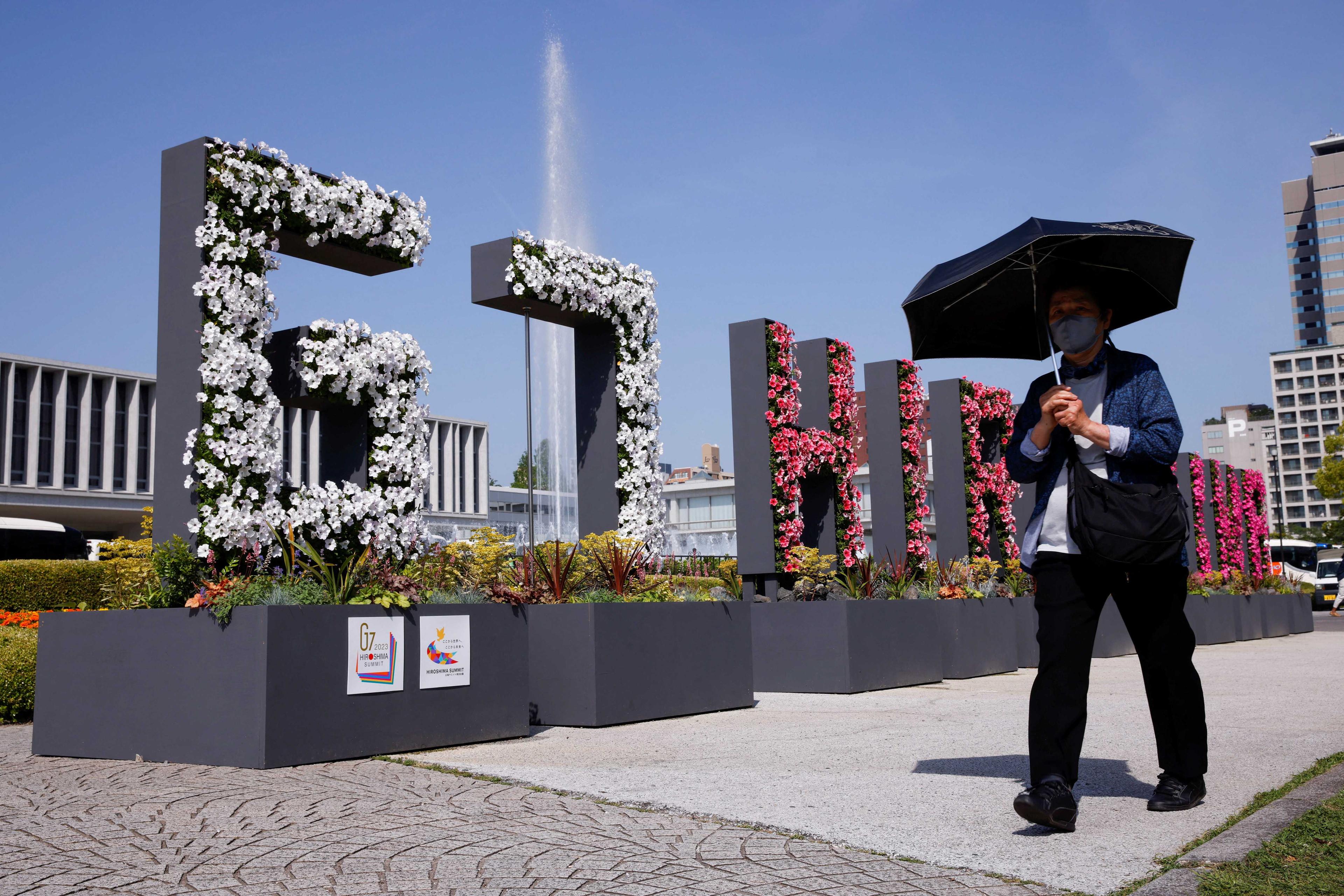 Seorang wanita terpaksa menggunakan payung sewaktu berjalan melintasi susunan pokok hiasan yang membentuk perkataan ‘G7 Hiroshima’ berhampiran Muzium Memorial Keamanan, menjelang Sidang Kemuncak G7, di Hiroshima, Jepun, 17 Mei. Gambar: Reuters