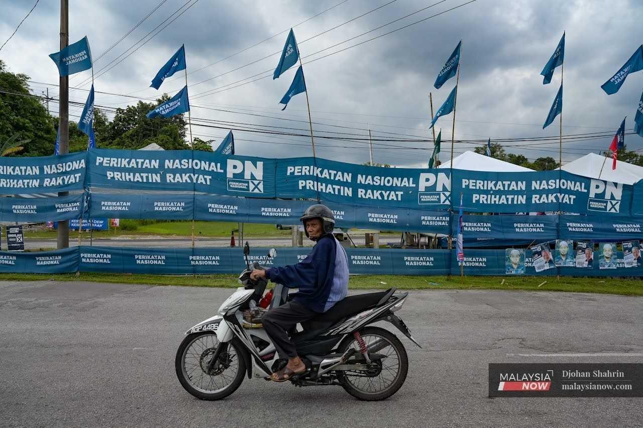 A motorcyclist passes a road decked out in Perikatan Nasional flags and banners.