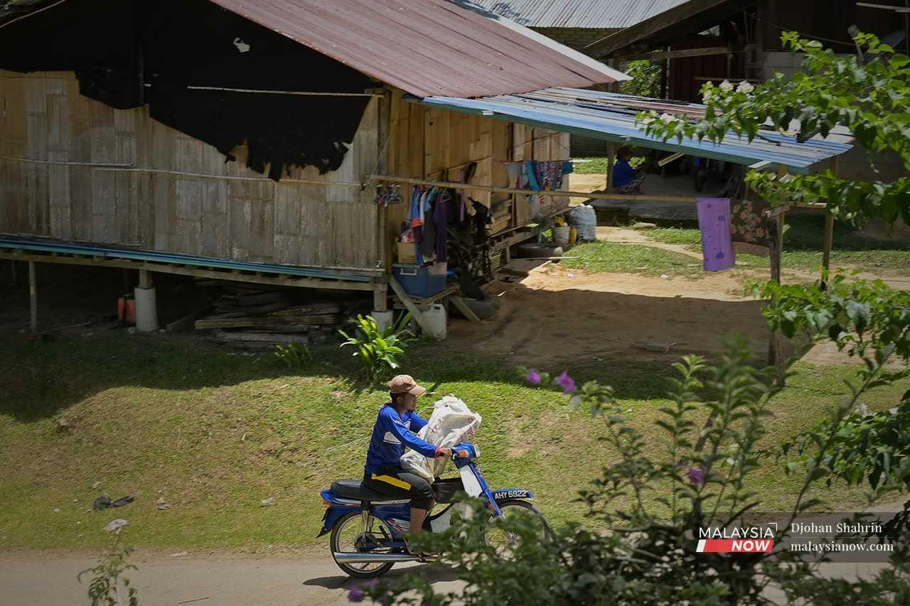An Orang Asli man rides his motorcycle past houses in Kampung Sungai Raba, Gerik in Perak.