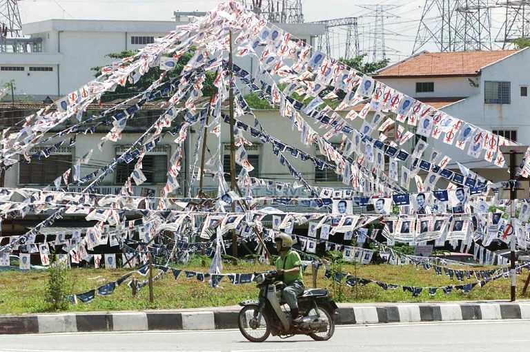 Gambar fail menunjukkan seorang penunggang motosikal melalui taman yang dipenuhi sepanduk kempen pilihan raya DAP dan Barisan Nasional di Kuala Lumpur, 25 November 1999. Gambar: AFP