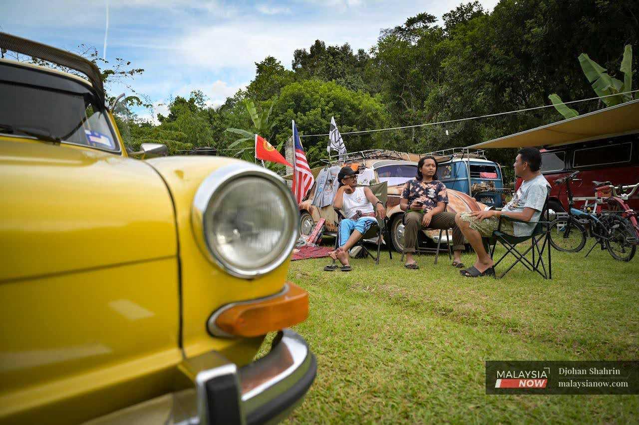 Participants sit on foldable chairs near their cars: a classic Fastback Type 3, Kombi, and Beetle. 
