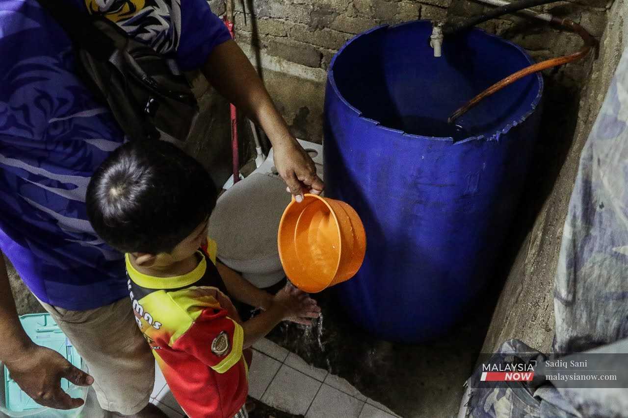 Anuar Mohd Akhir membantu anaknya mencuci tangan menggunakan air yang disimpan dalam tong di rumahnya di Kampung Padang, Hulu Langat.