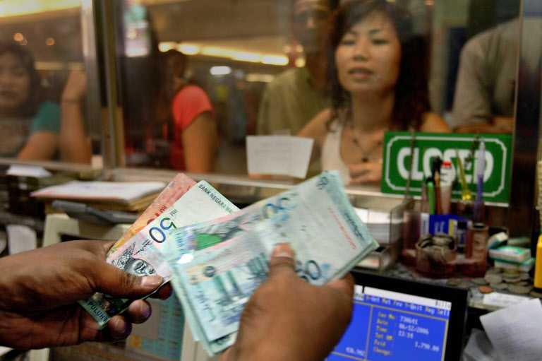 A money changer counts bank notes while customers wait at a foreign exchange booth in downtown Kuala Lumpur. Photo: AFP
