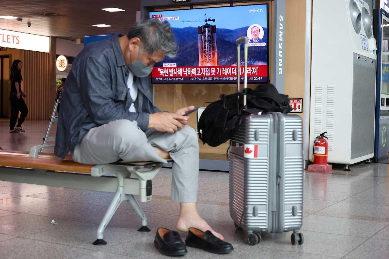 A man looks at his smartphone as a TV broadcasts a news report on North Korea firing what it called a space satellite toward the south, in Seoul, South Korea, May 31. Photo: Reuters