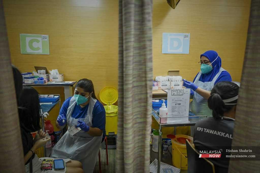 A health worker explains the vaccination process to a teenager while another prepares a booster dose to be given to a medical frontliner in this file picture taken at KPJ Tawakkal in Jalan Pahang, Kuala Lumpur.